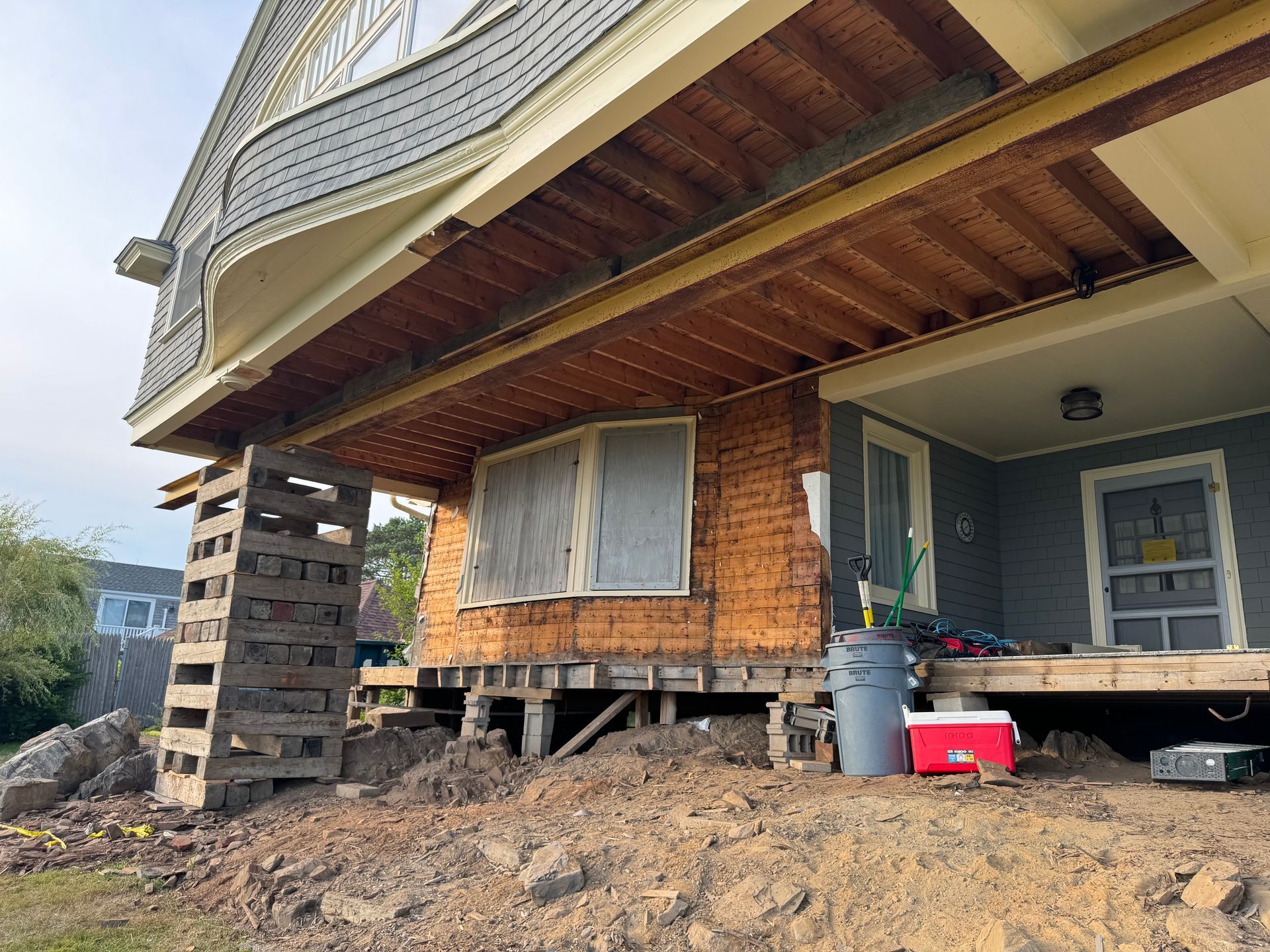House raised on wooden supports for renovation. Brown and grey construction materials.
