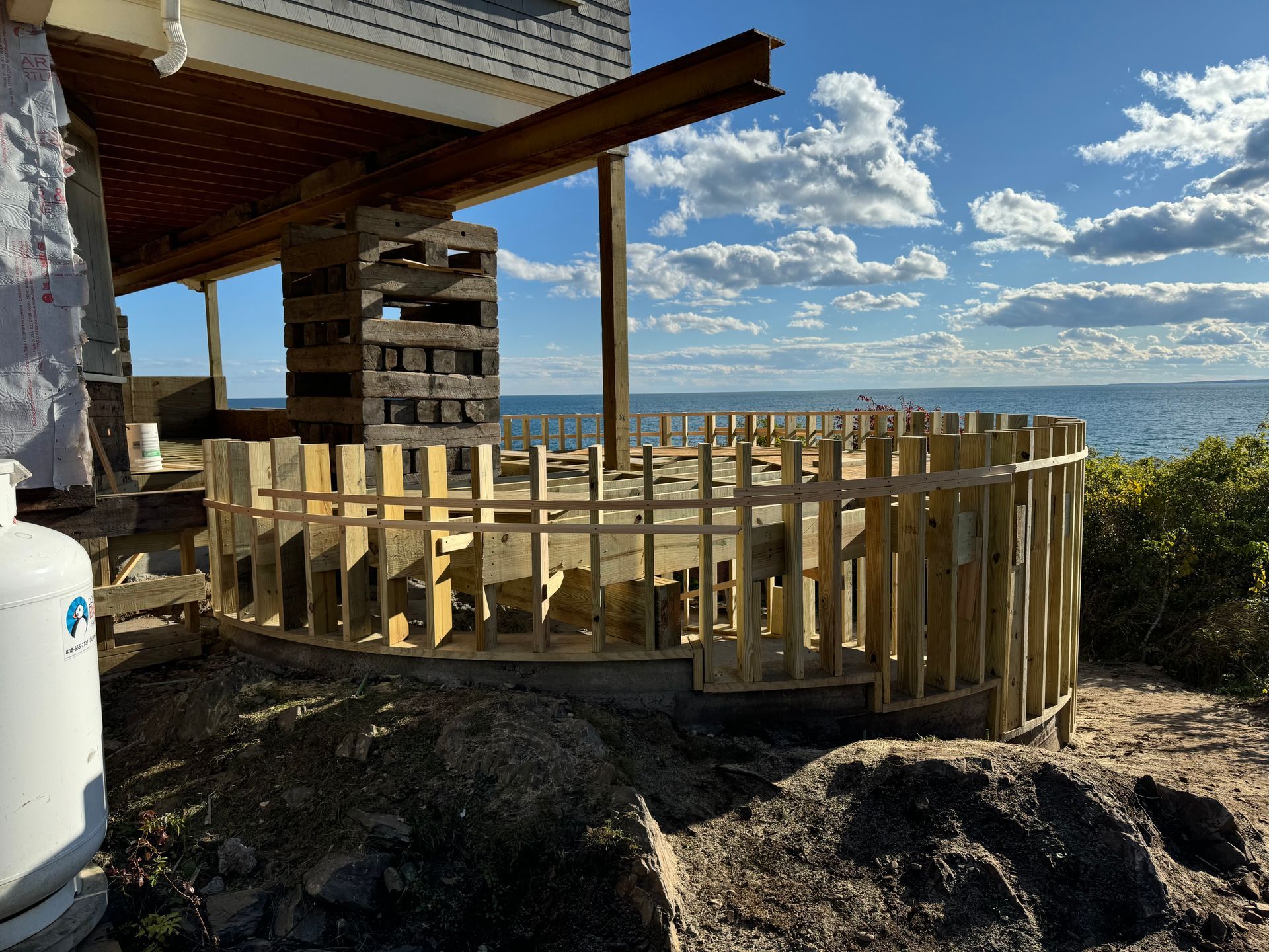 Deck construction site overlooking the ocean; wooden frame, support beams, blue sky and water.