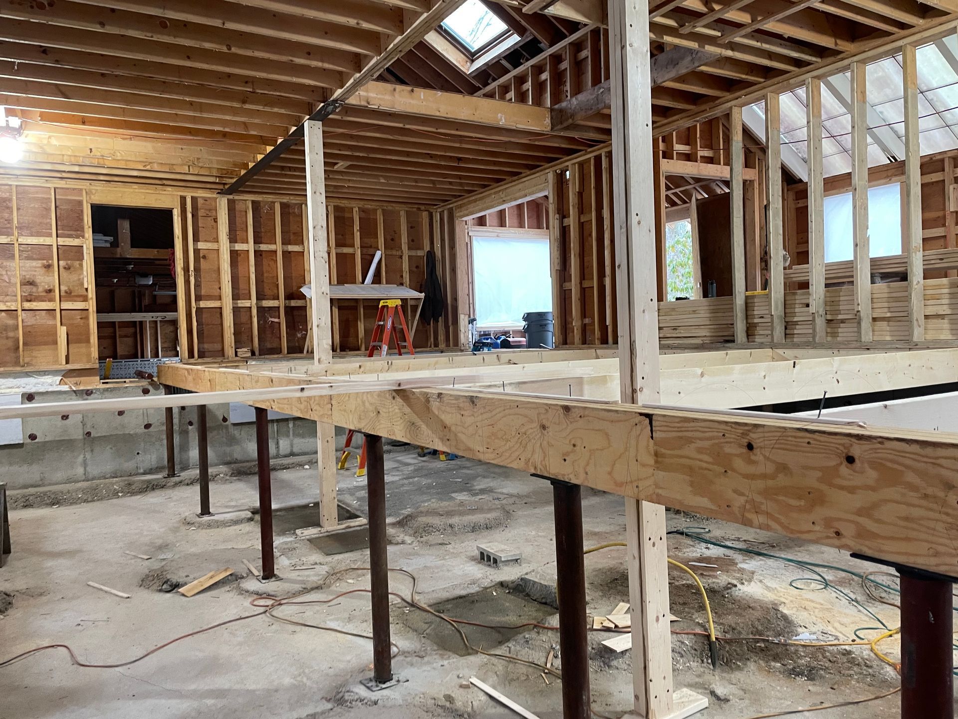 Interior of a building under construction. Exposed wooden framing, a partially built second level, and a concrete floor.