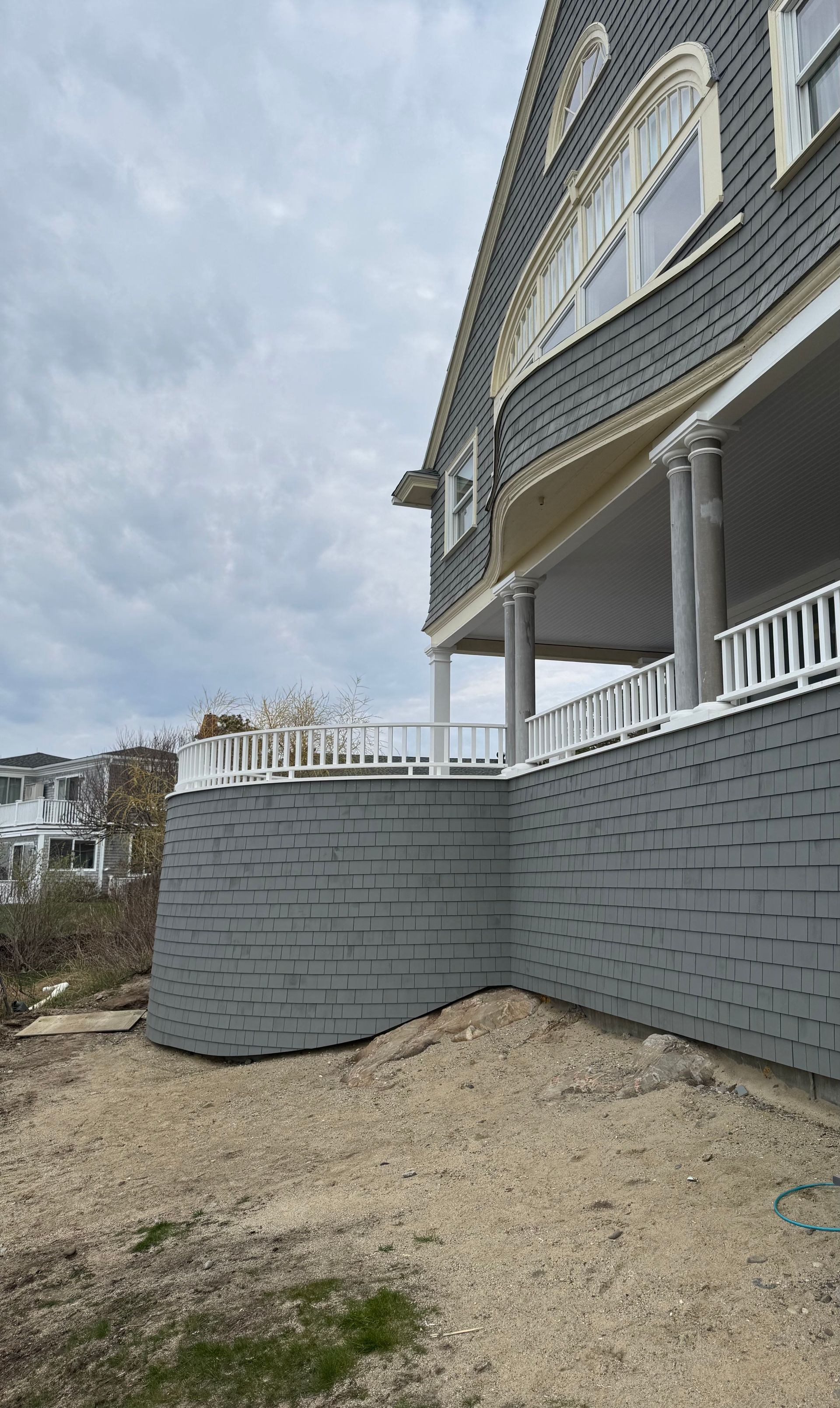 Gray house with brick retaining wall and white porch railing, under cloudy sky.