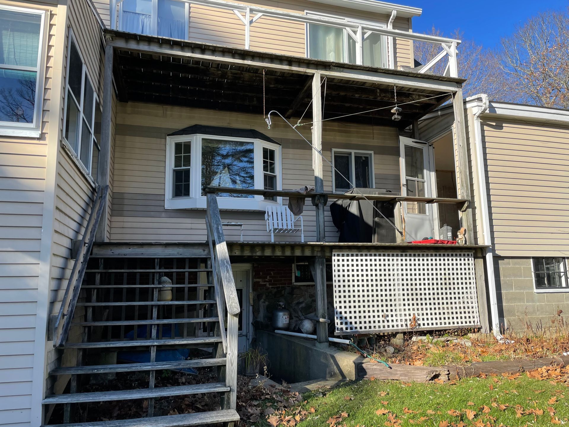 Exterior view of a multi-level house with a deck, stairs, and a bay window. Green lawn and blue sky.