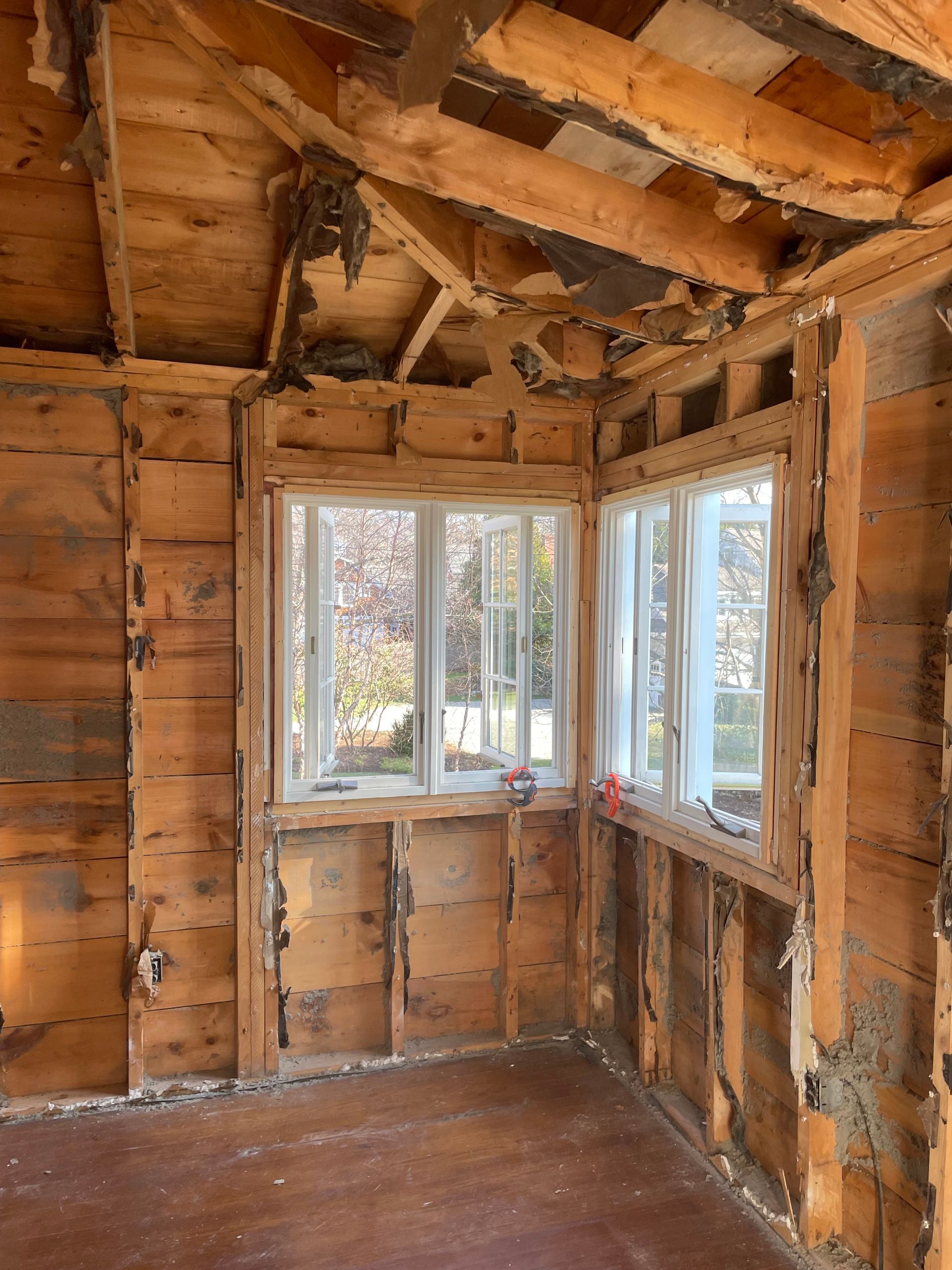 Interior room under renovation, wood walls and ceiling, white framed windows.