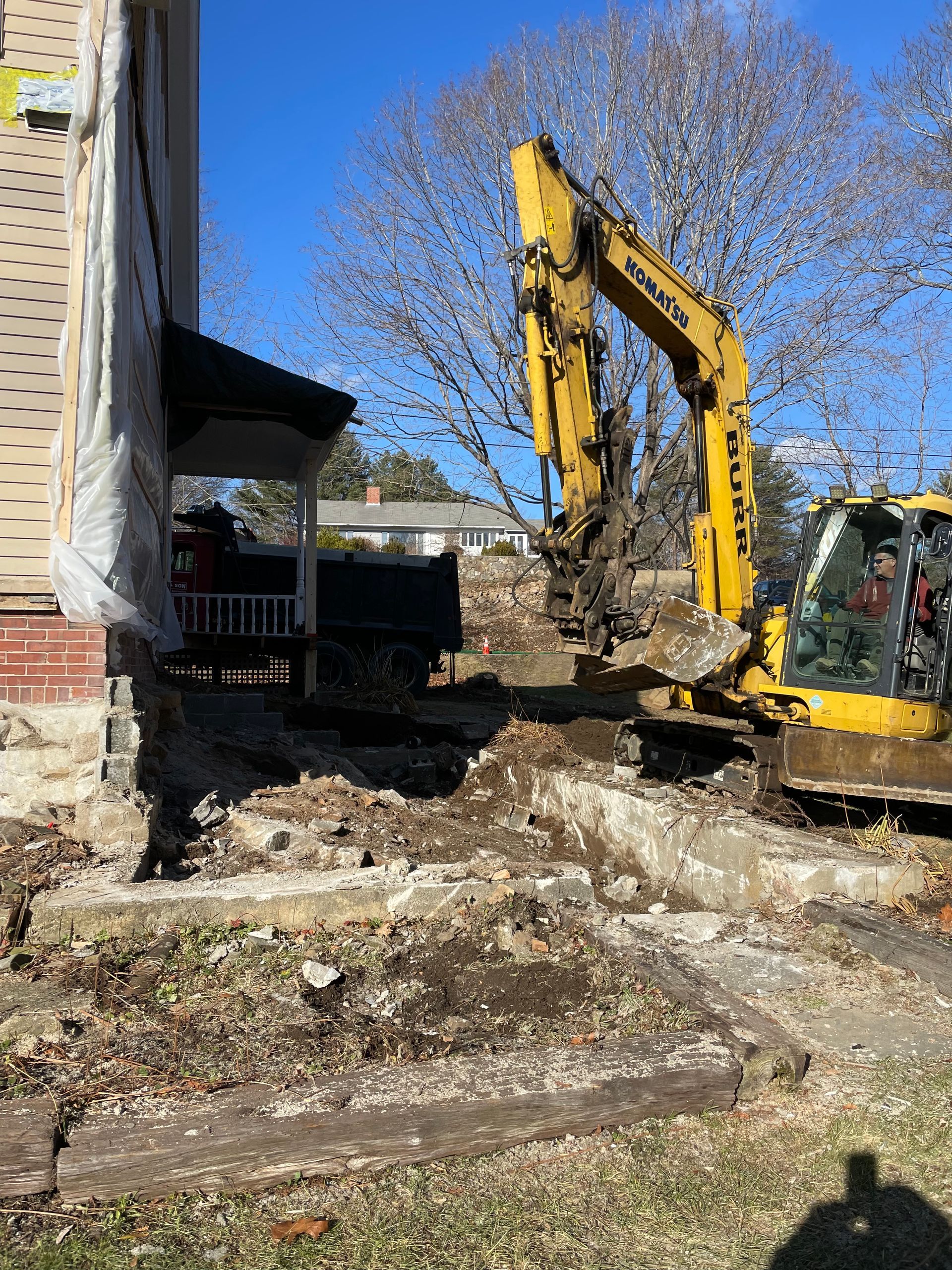Yellow excavator demolishing concrete steps next to a house under construction.
