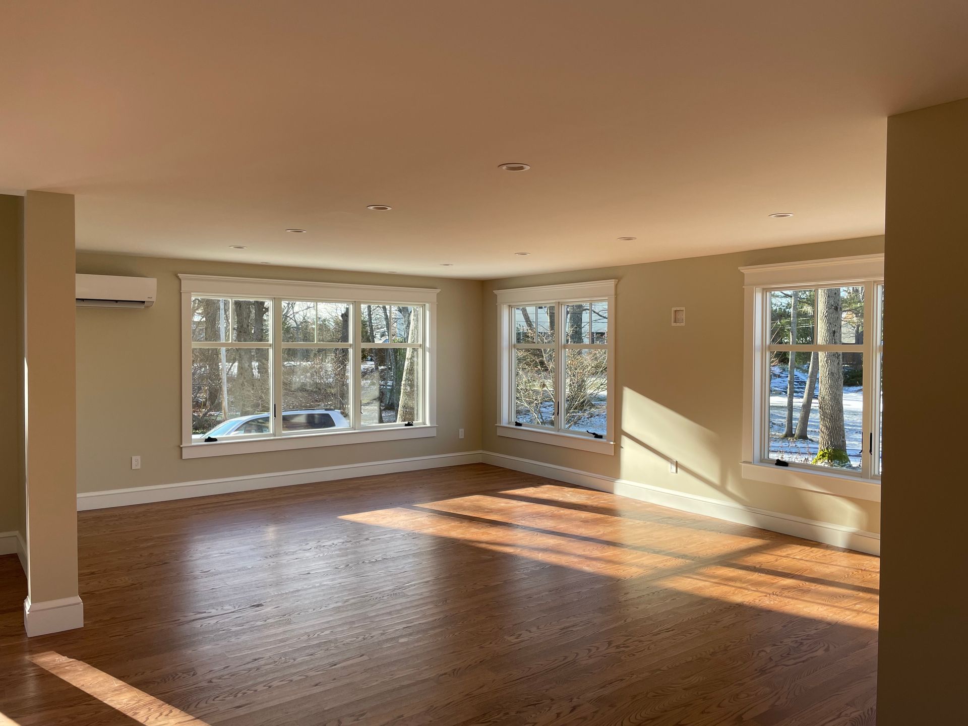 Empty sunlit room with hardwood floors and multiple white-framed windows.
