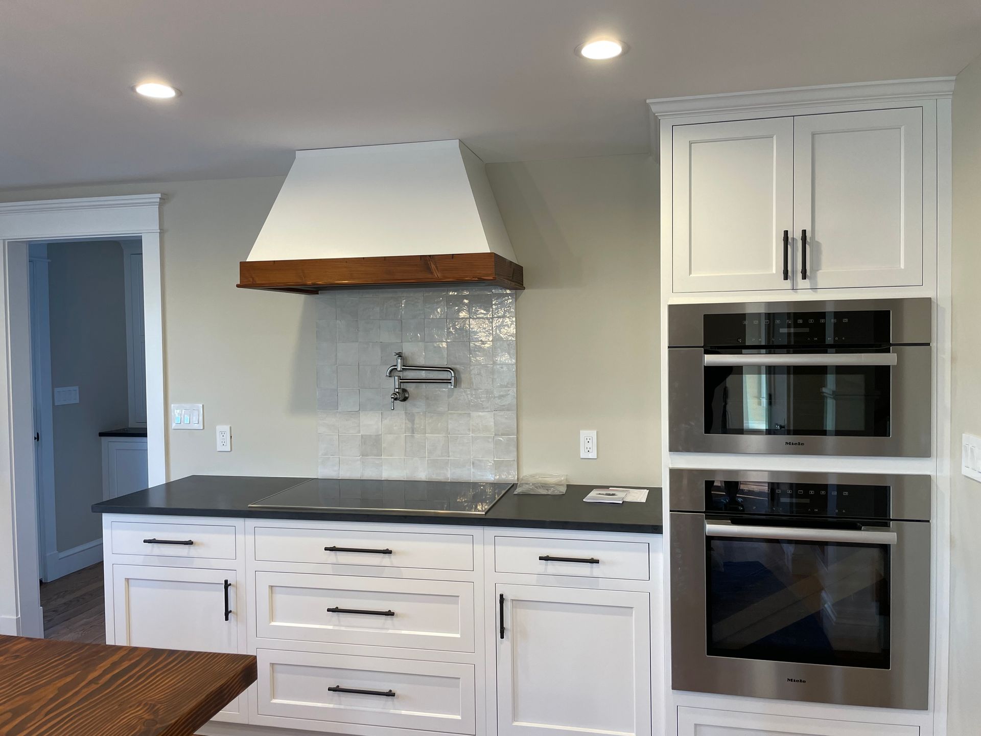 White kitchen with a stove, hood, and built-in ovens.