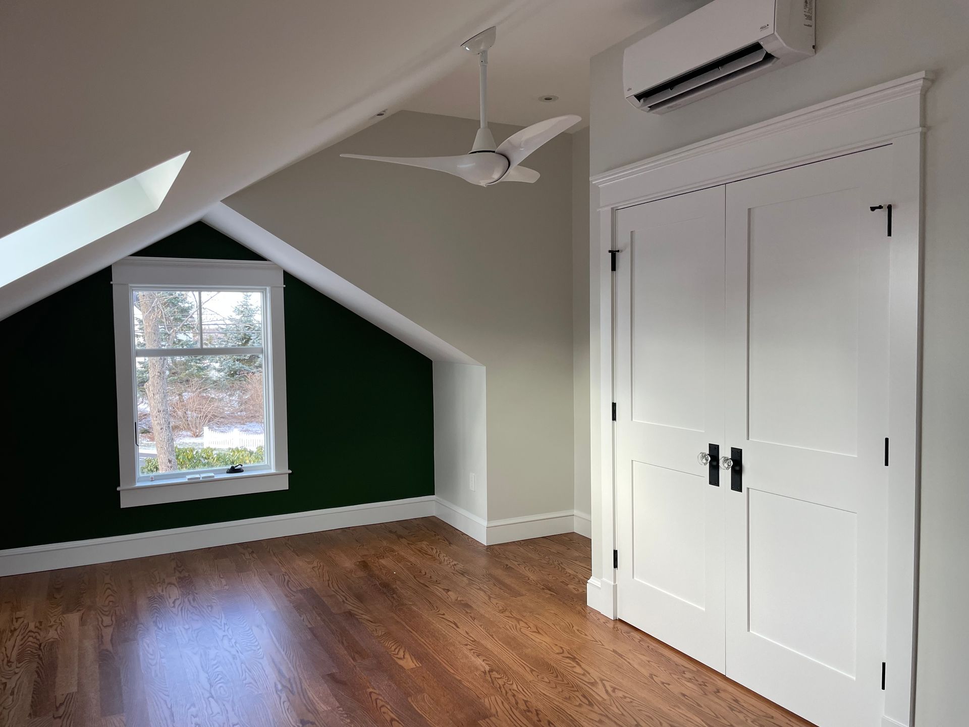 Bedroom with hardwood floor, green accent wall, white closet doors, and a window.