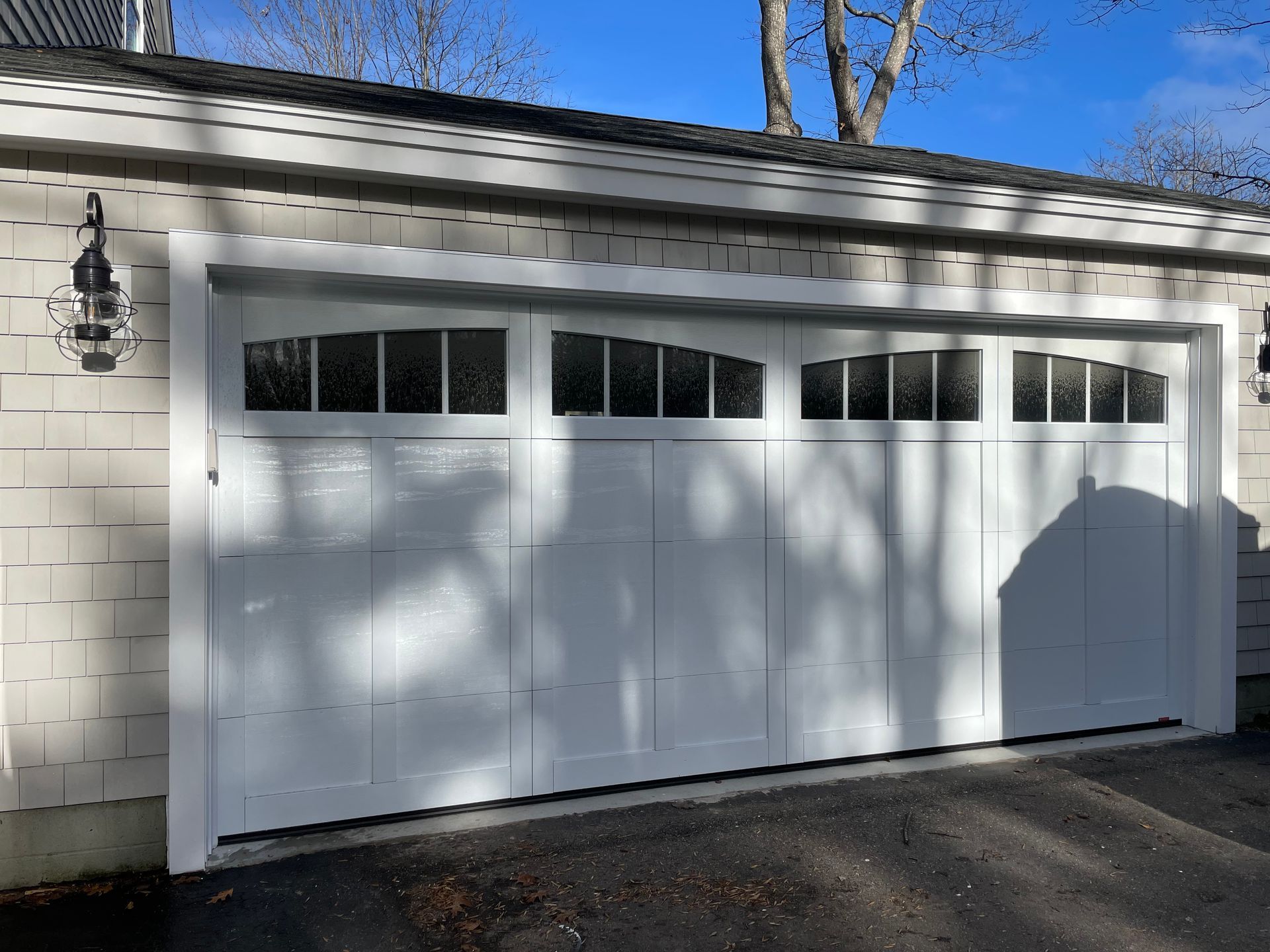 White garage door with arched window panels; a light fixture hangs on the left.