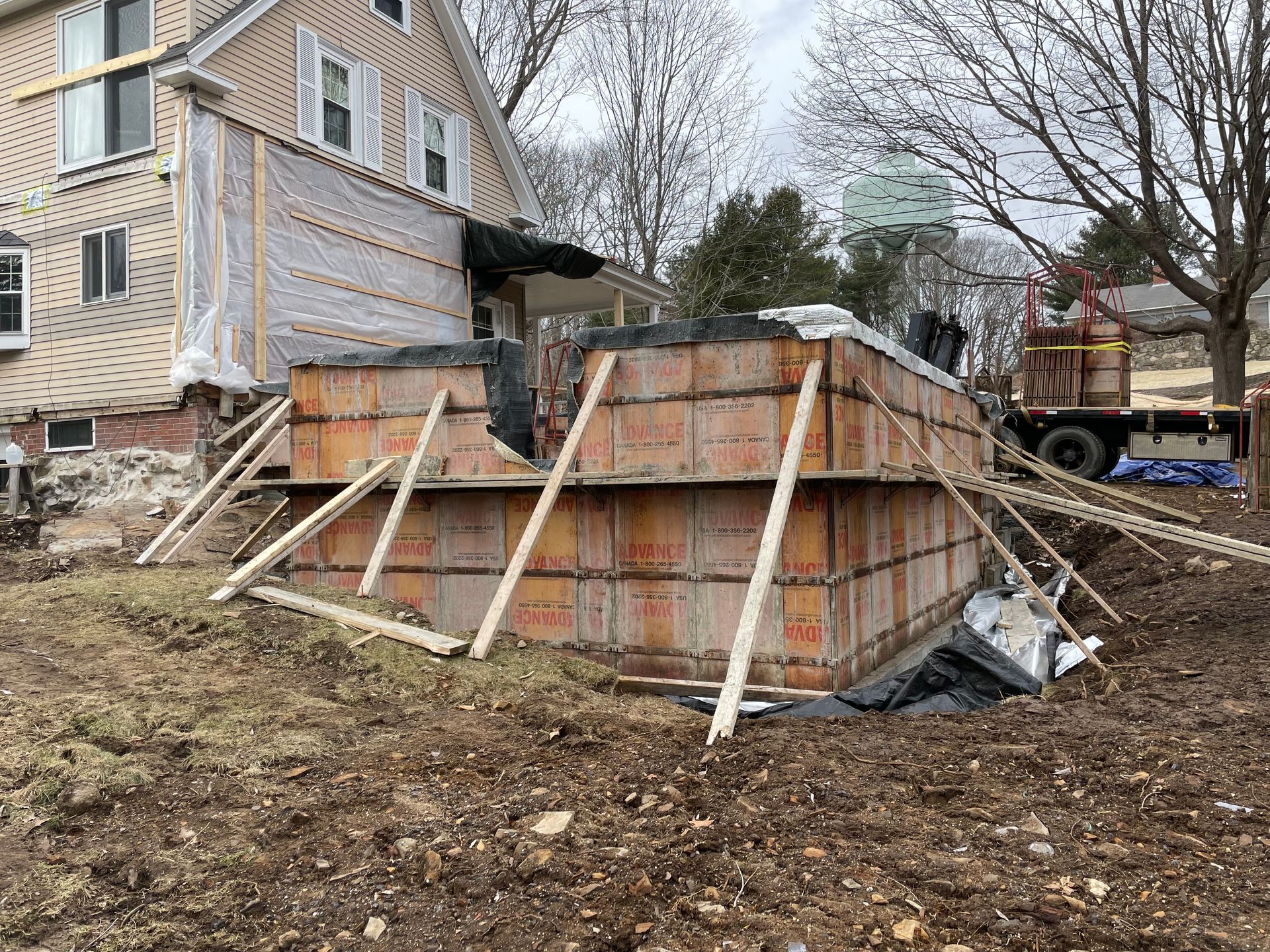Construction site: orange concrete forms supported by wooden braces, near a house.