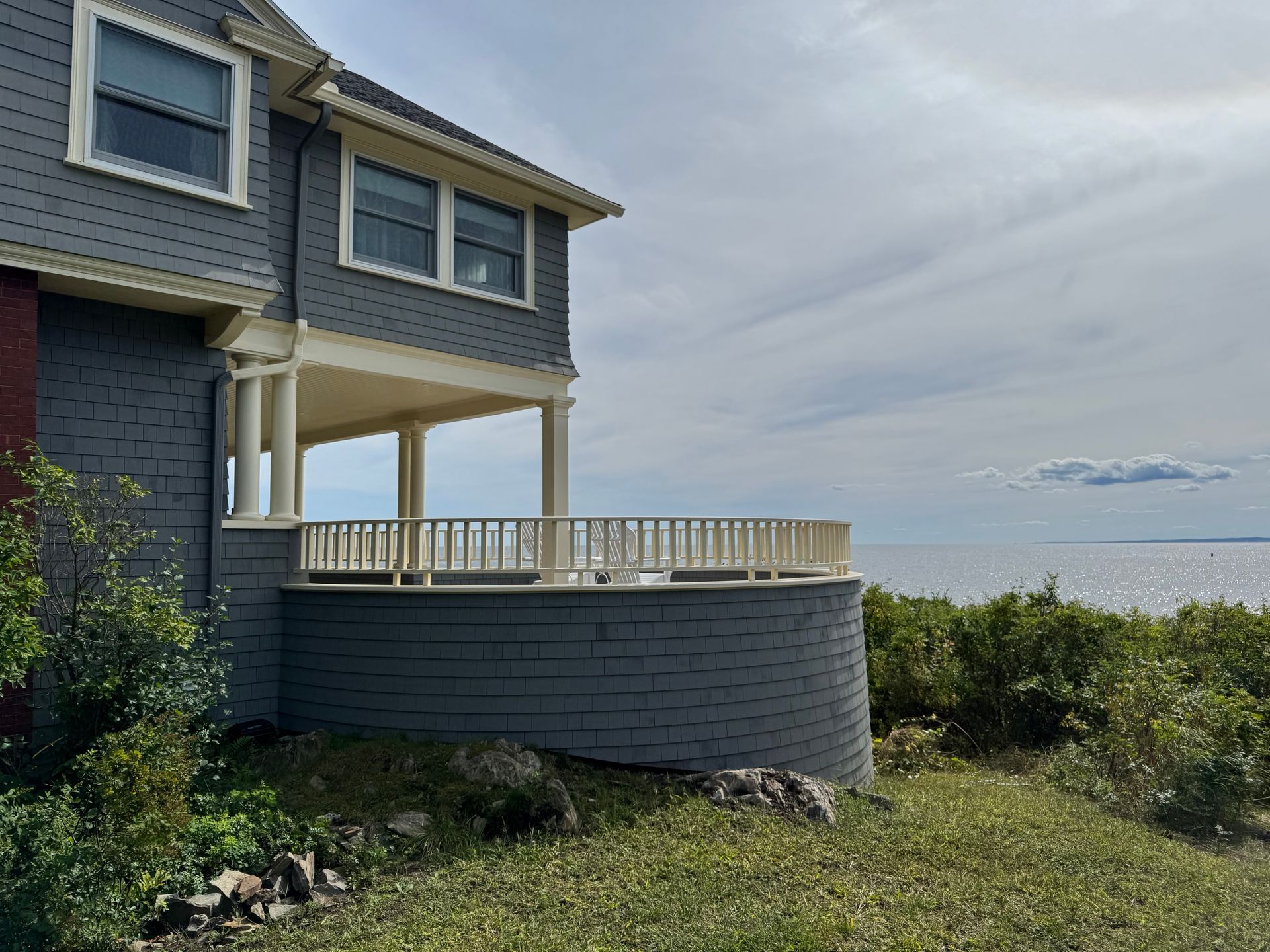 Gray house with porch overlooking ocean. Overcast sky.