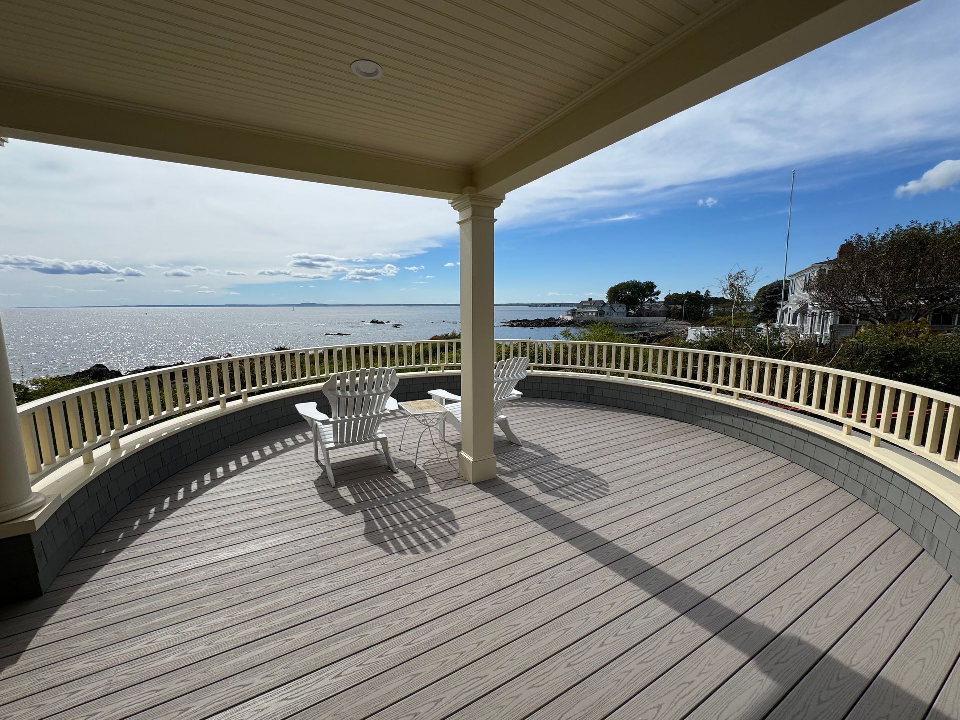 Curved wooden deck with white railing overlooking a body of water under a bright sky.
