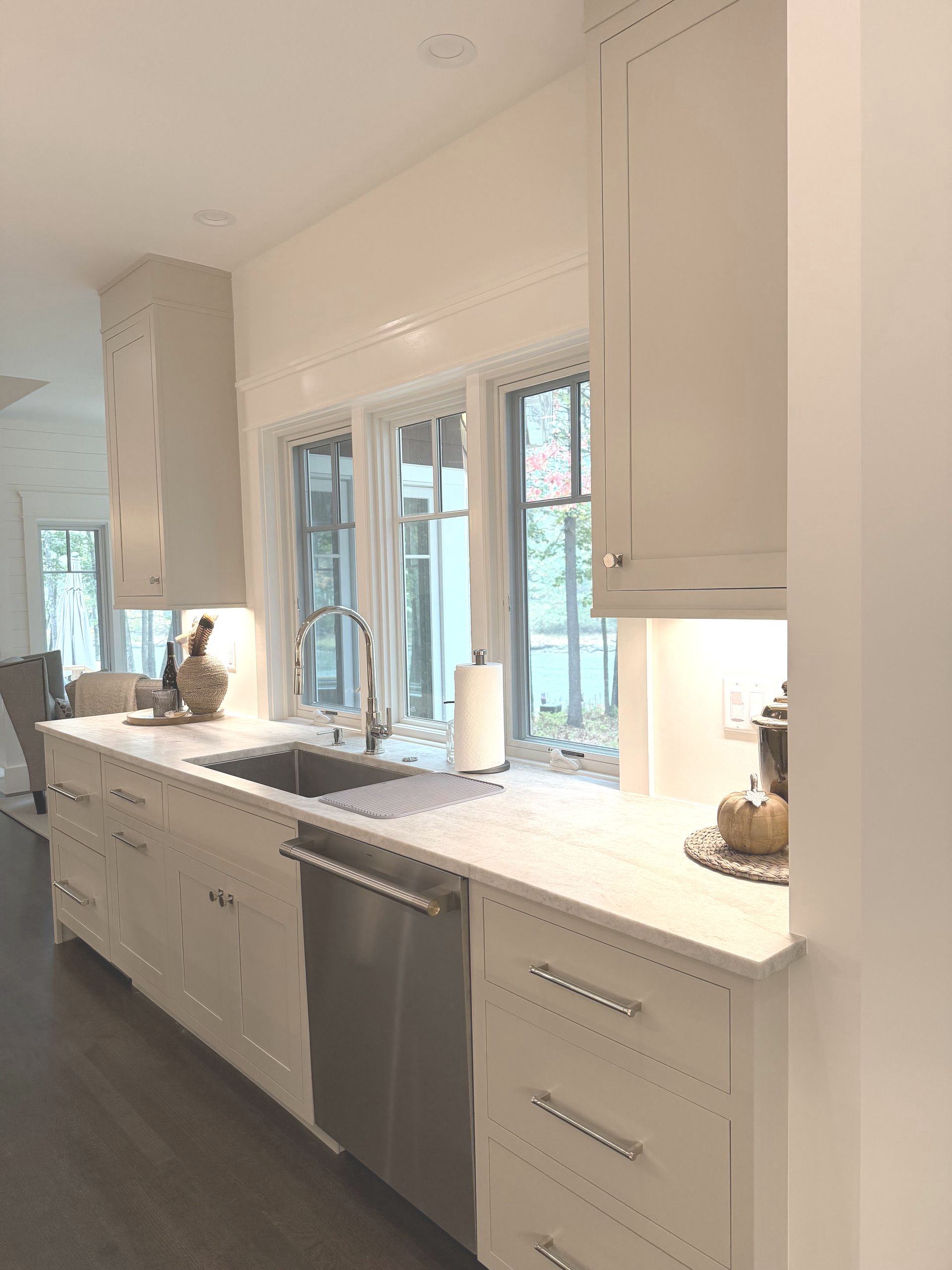 White kitchen with cabinets, sink, and stainless steel dishwasher under a window.