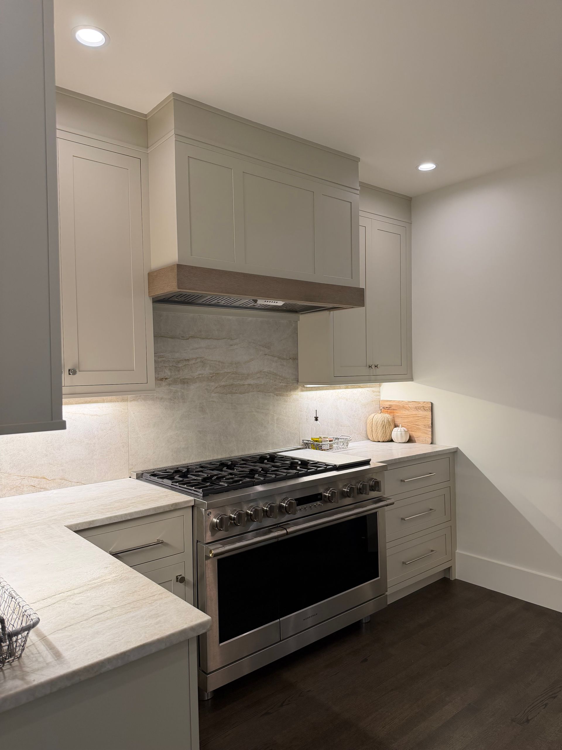 Kitchen with light gray cabinets, stainless steel stove, and wooden range hood.