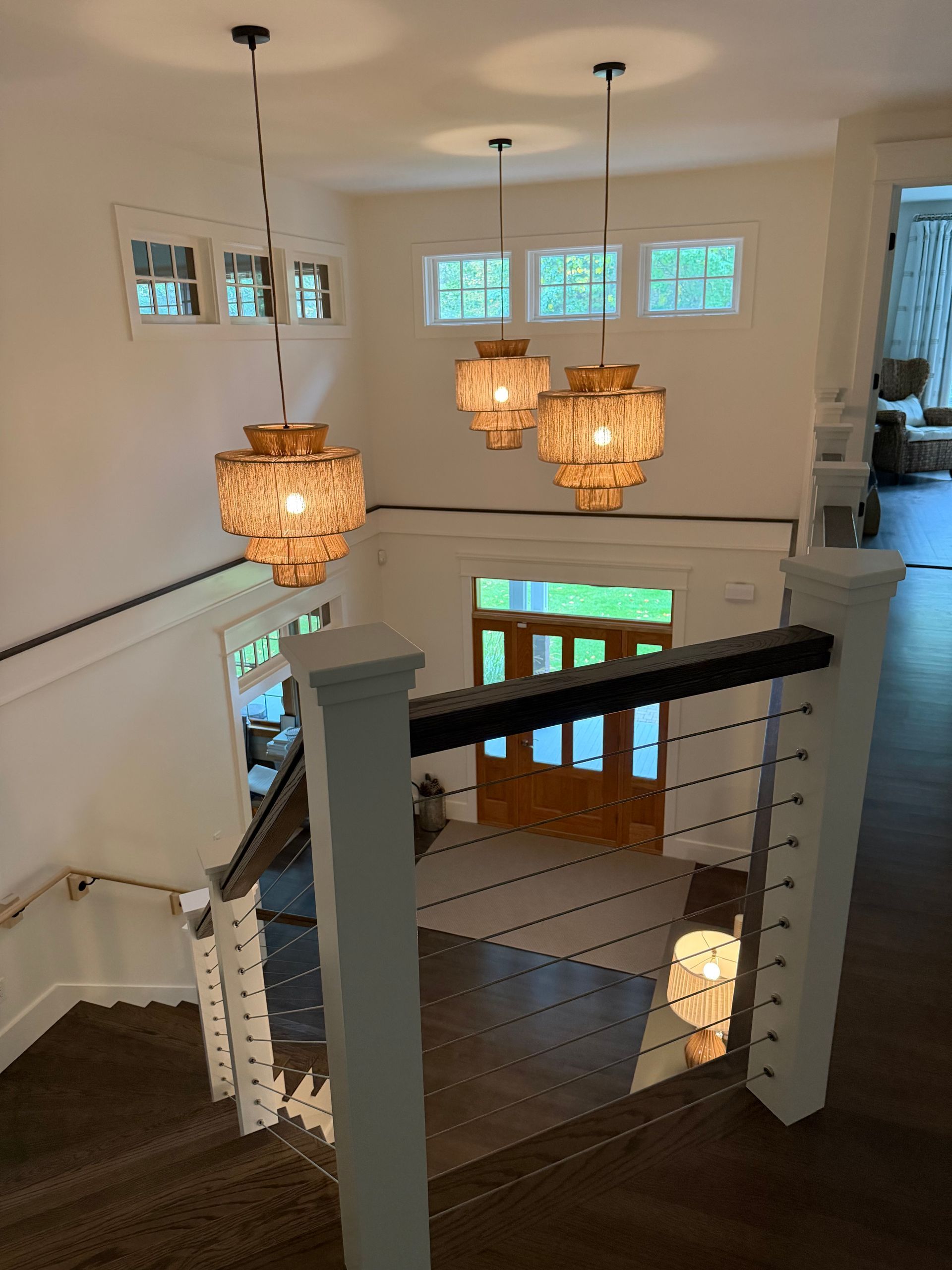 Elegant entry hall with staircase, three pendant lights, and dark wood floors.