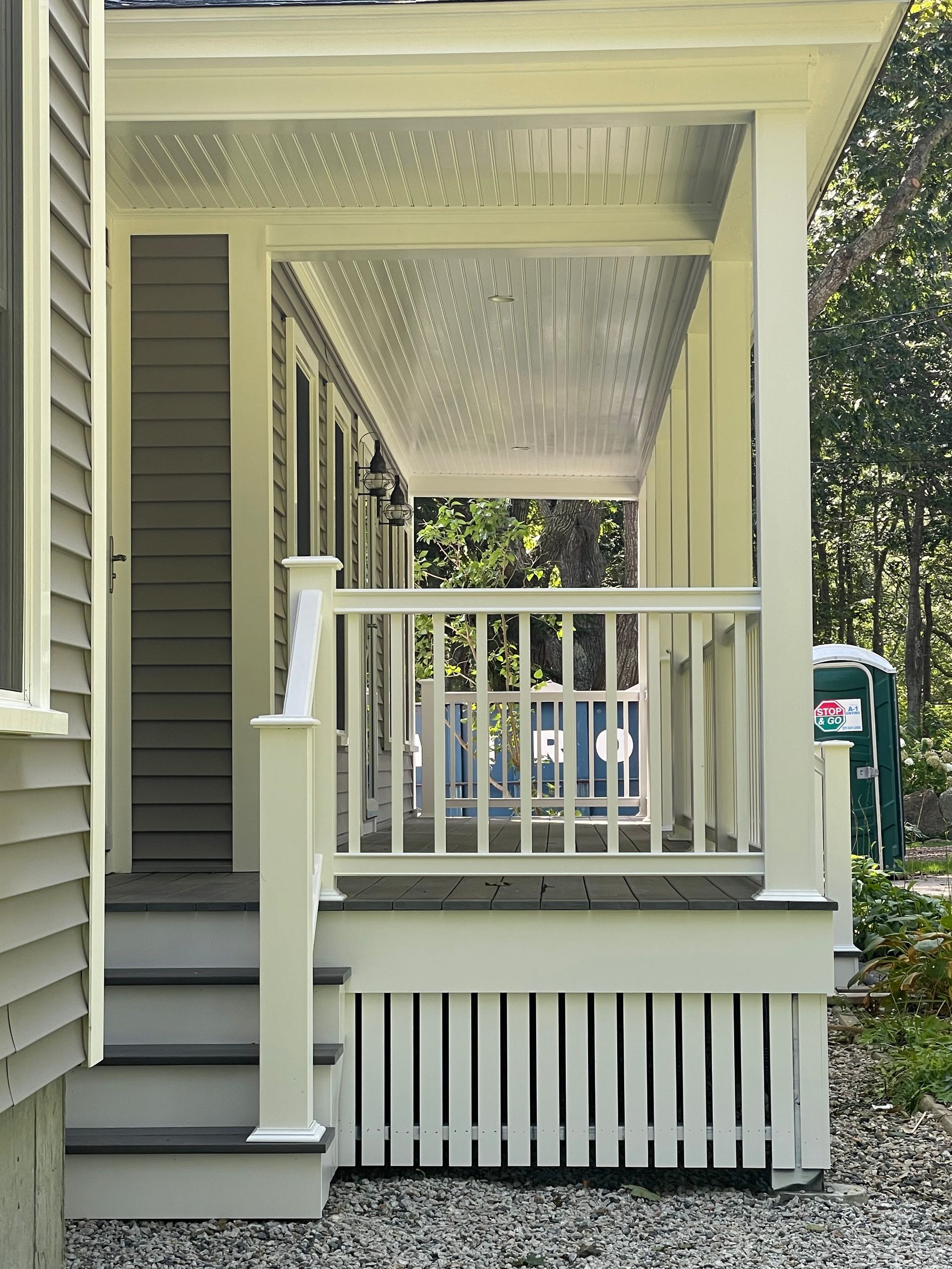 Covered porch with white railings, columns, and soffit. Gray stairs and siding.