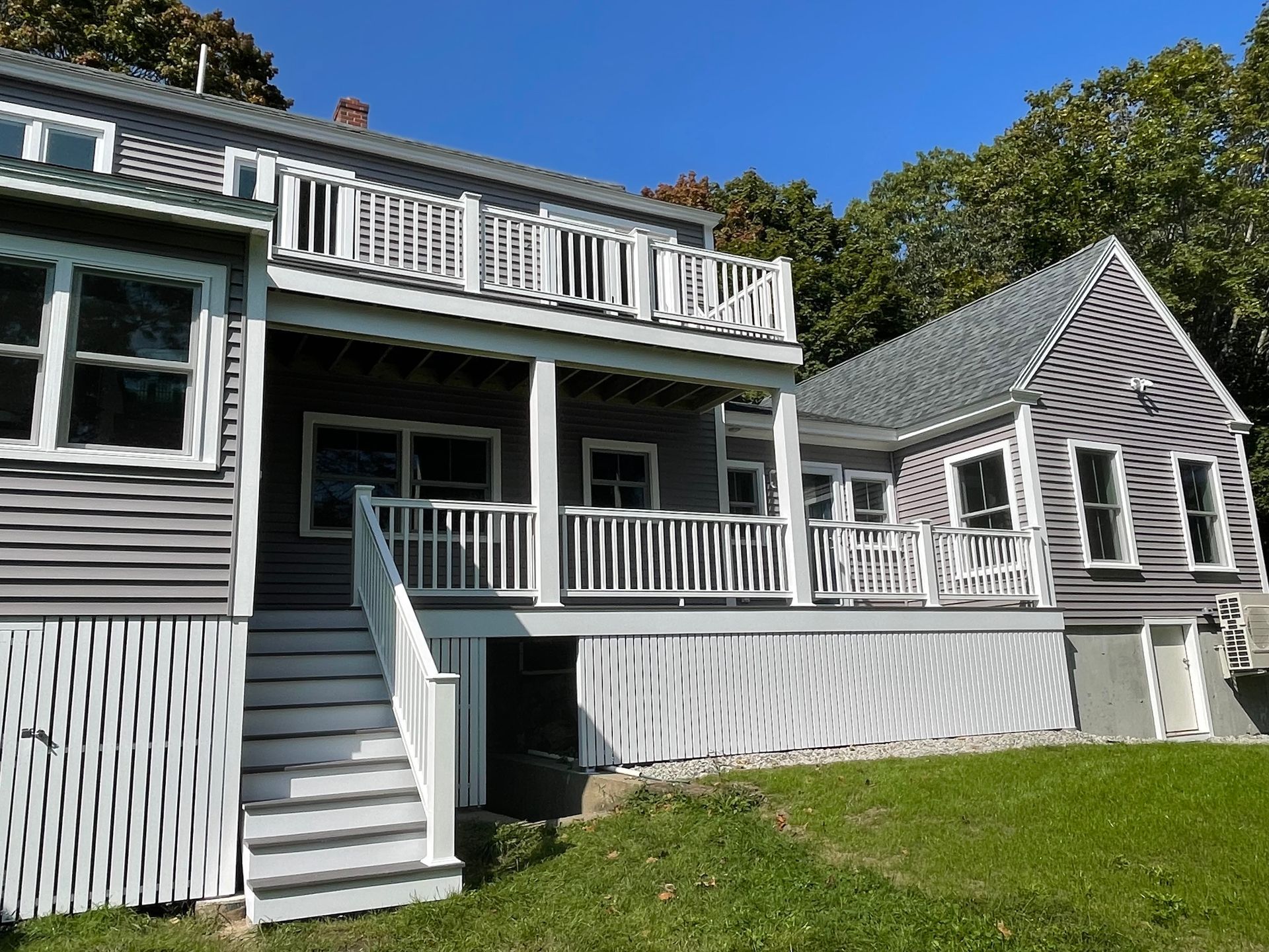 Two-story gray house with white railings, stairs, and a deck, under a clear blue sky.