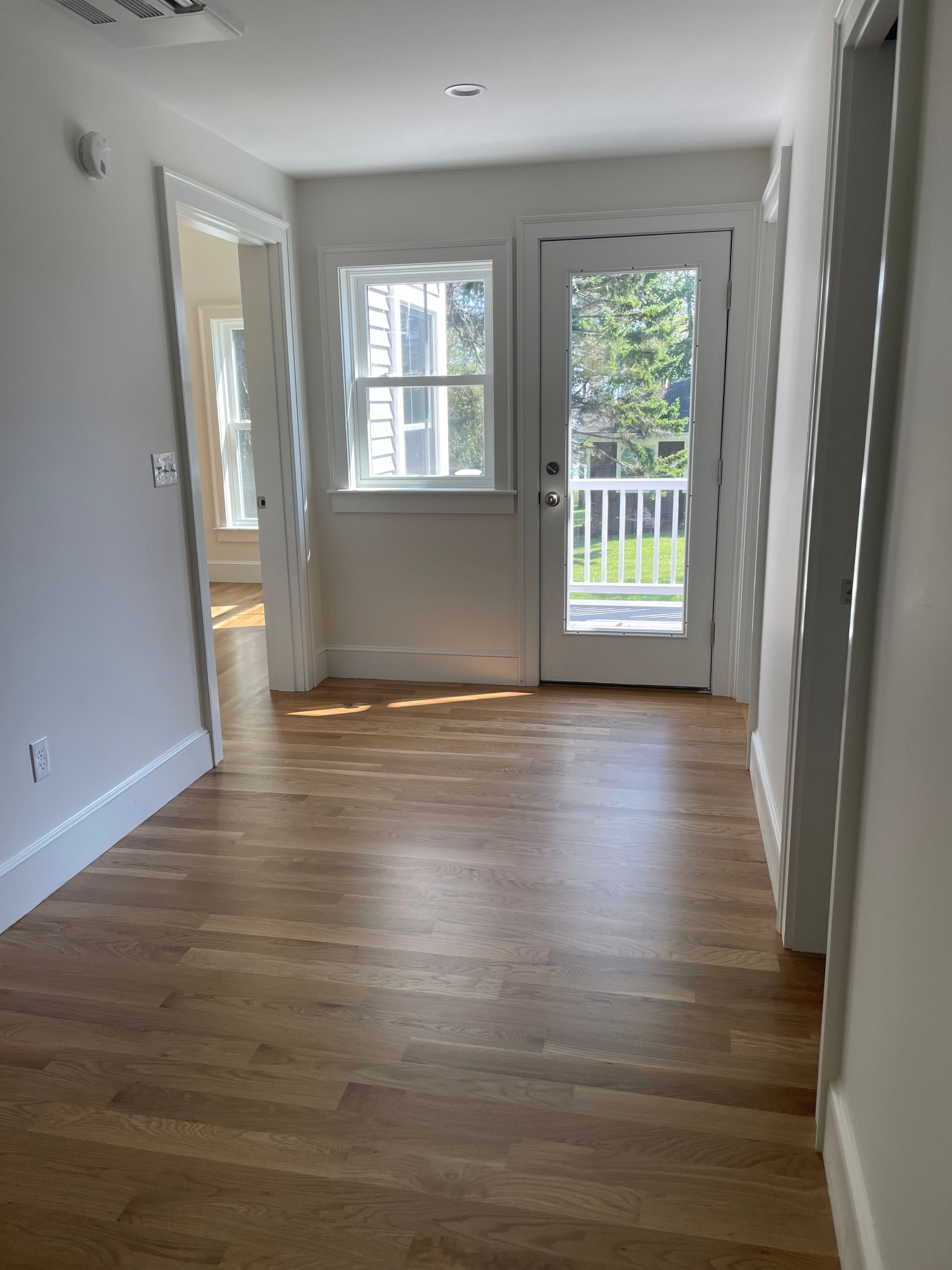 Hallway with hardwood floor leading to a window and glass door; white walls and trim.