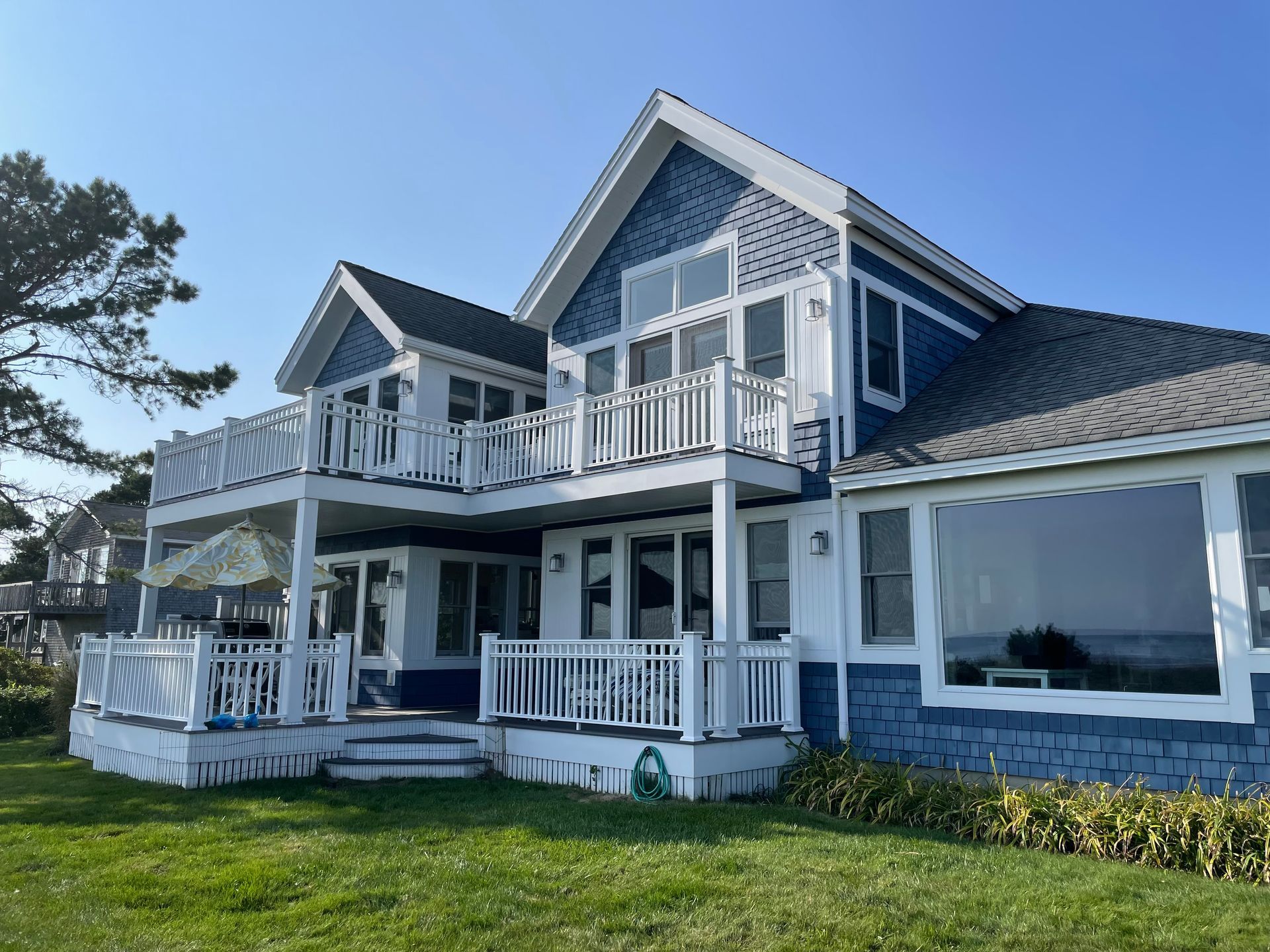 Blue and white beach house with two balconies, green lawn, and ocean view.