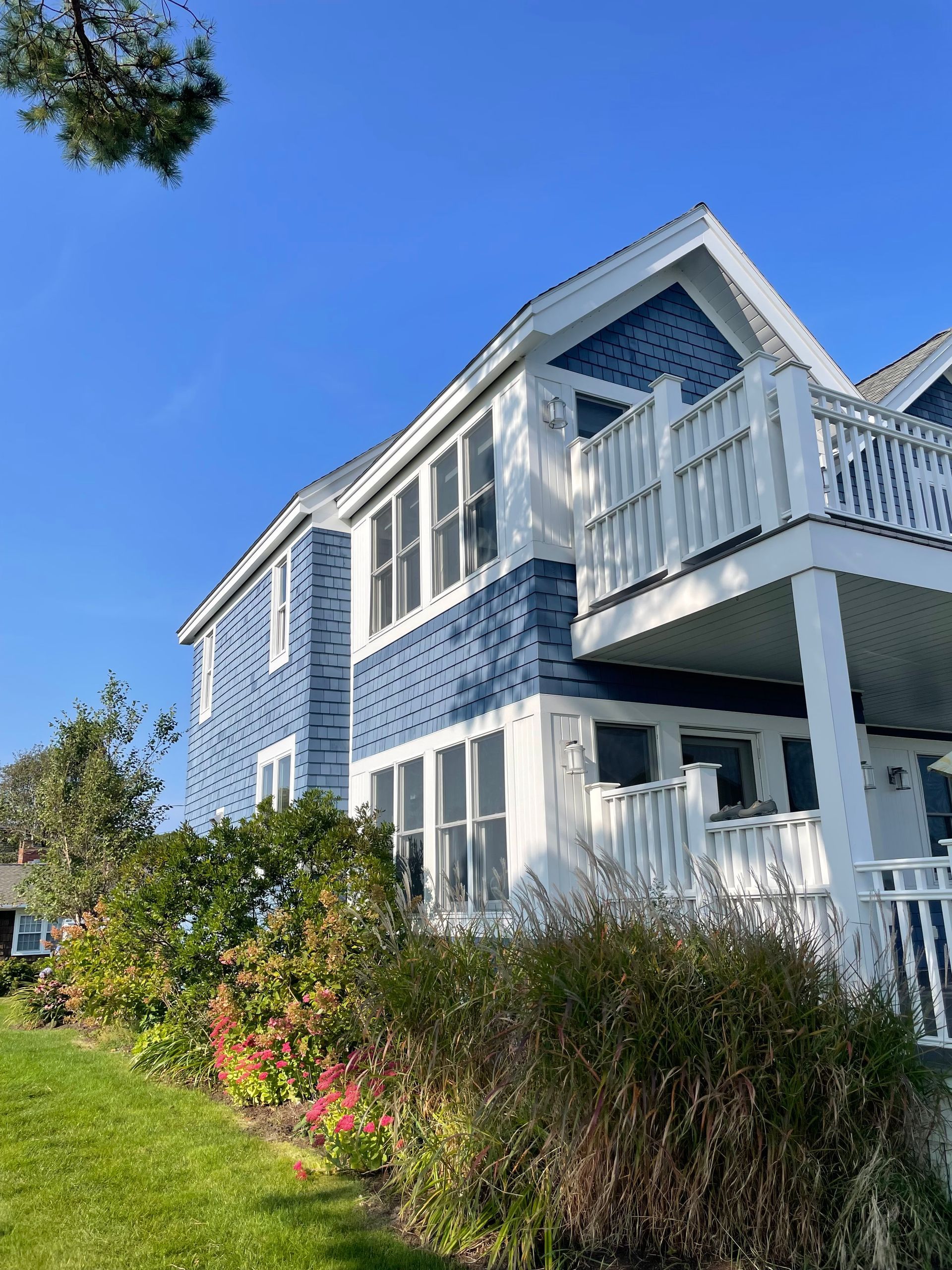 Blue and white multi-story house with balcony and windows under a clear blue sky.
