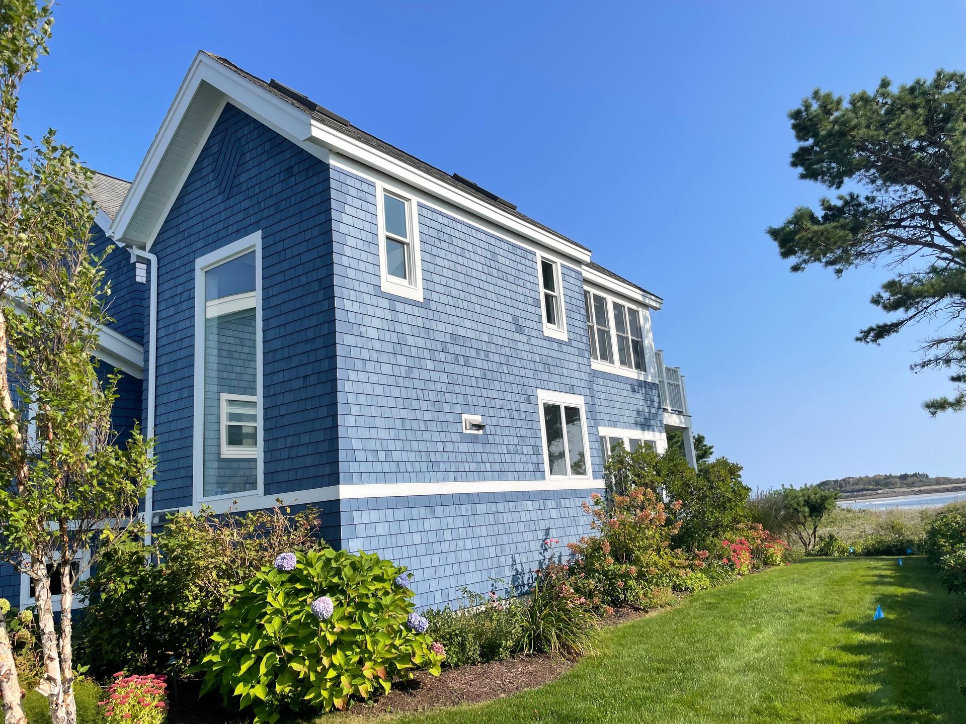 Blue-sided house with white trim, windows, and green lawn. Clear blue sky.