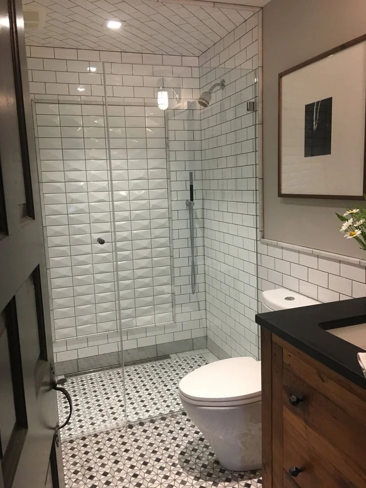 Bathroom with white brick tile shower, patterned floor, toilet, vanity, and framed art.