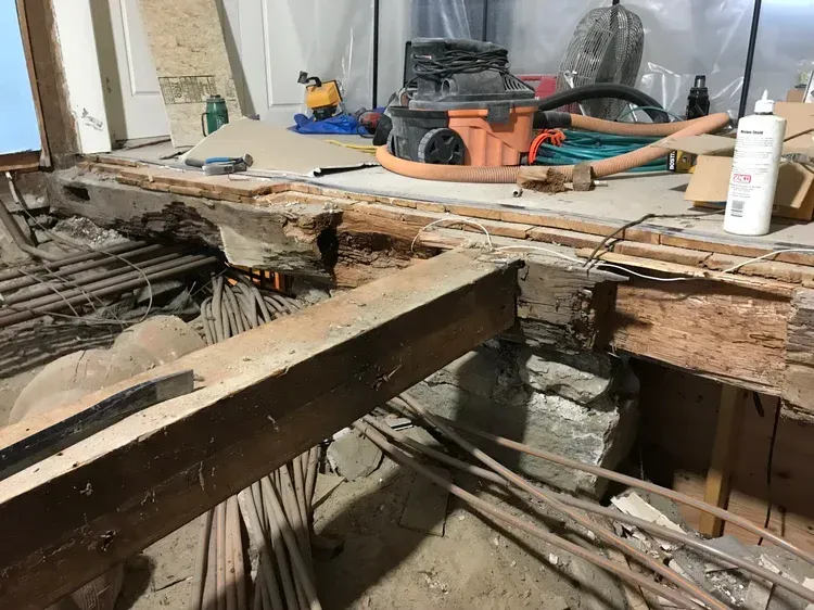 Interior view of a construction site. Damaged wood beams and debris on the floor, vacuum cleaner, and tools.