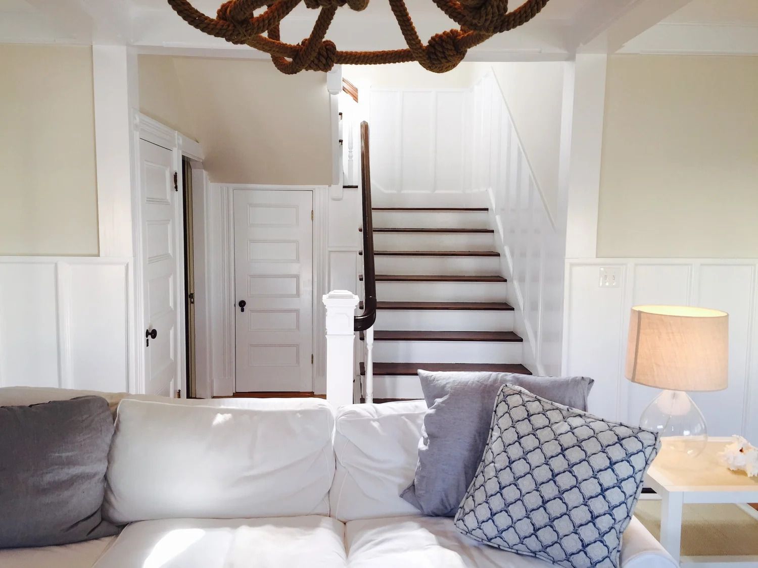 White living room with sofa, staircase, and rope chandelier.