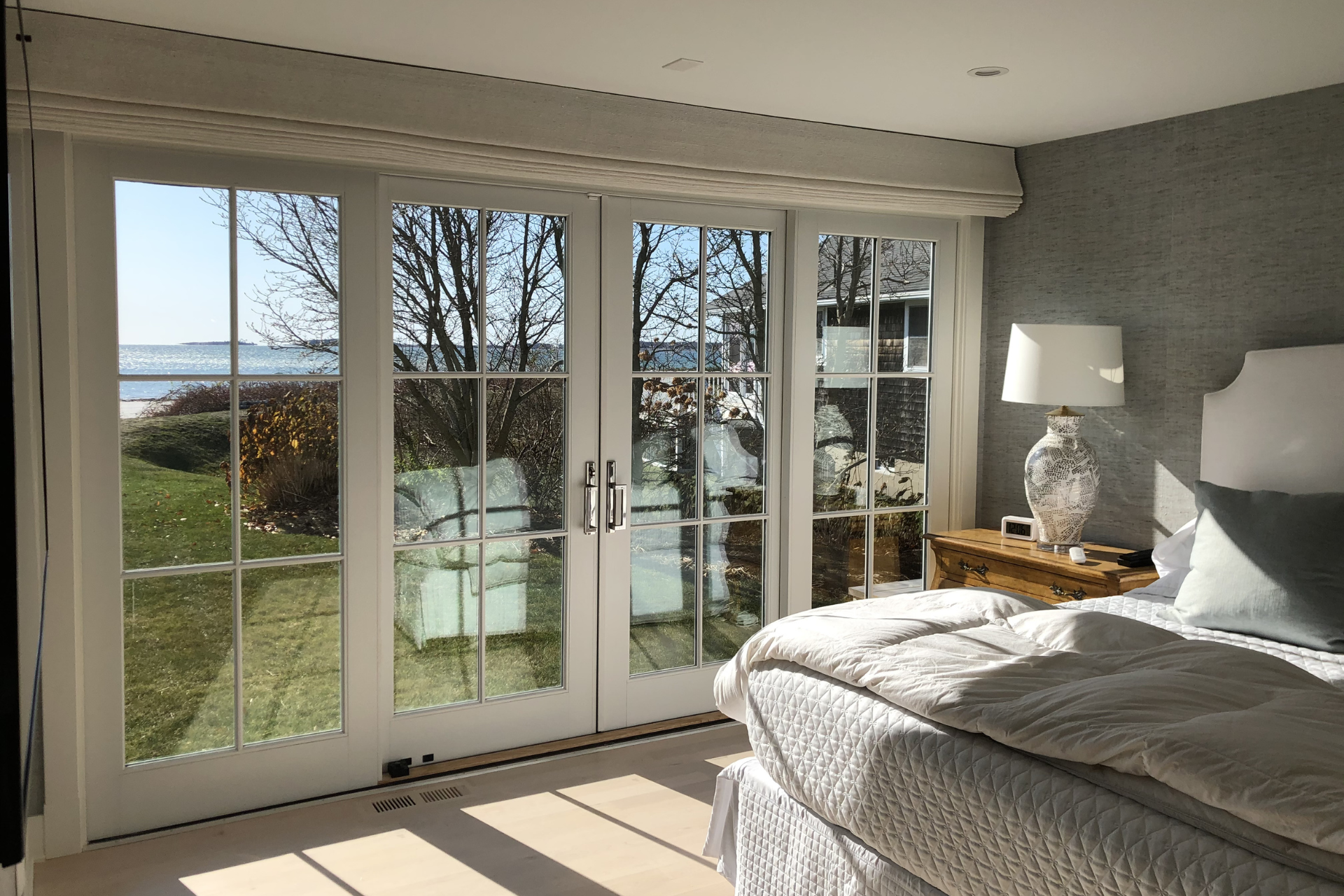 Bedroom with white doors, overlooking a sunny beach view. Bed, lamp, and neutral color scheme.
