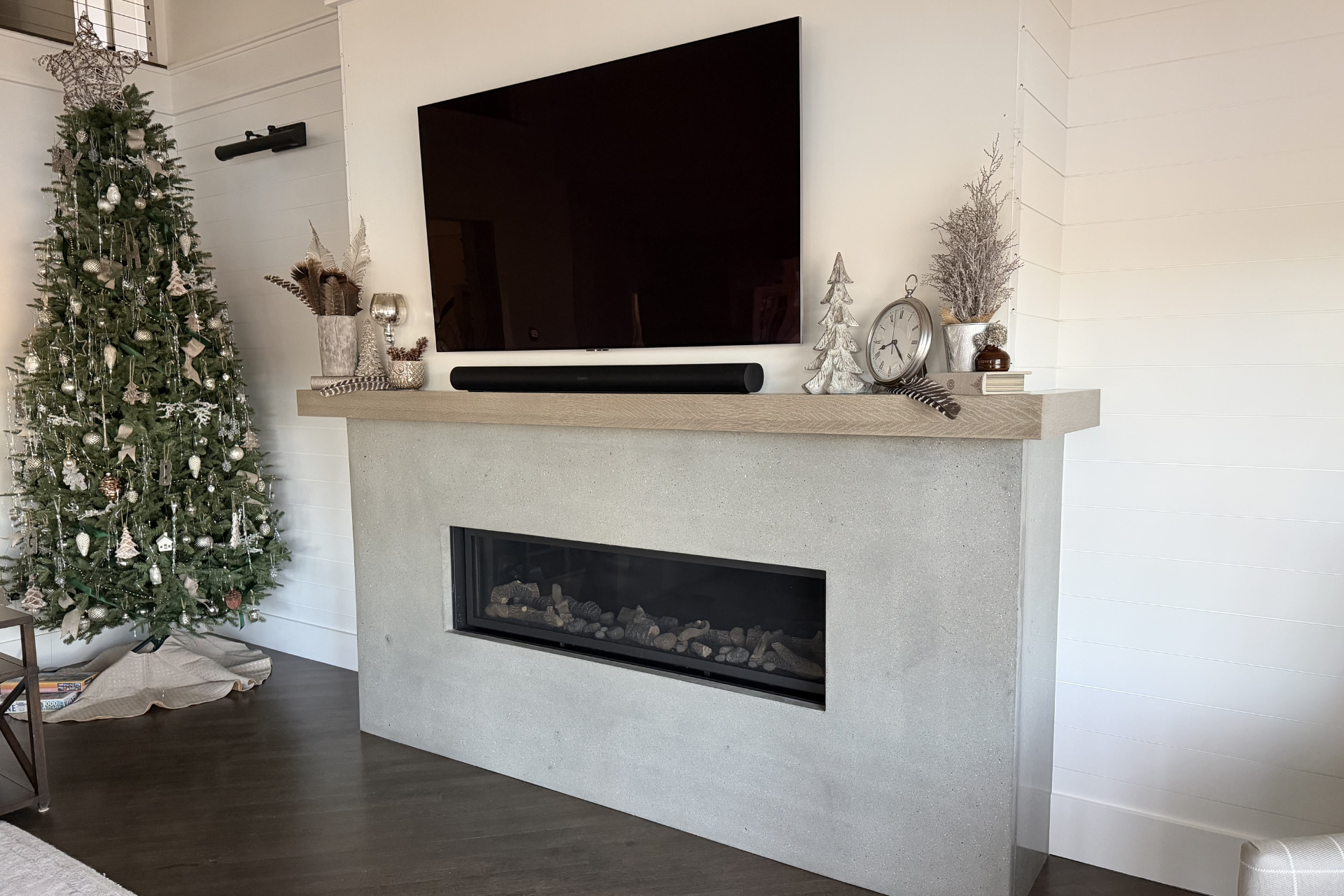 A decorated Christmas tree next to a fireplace with a mounted TV and soundbar.