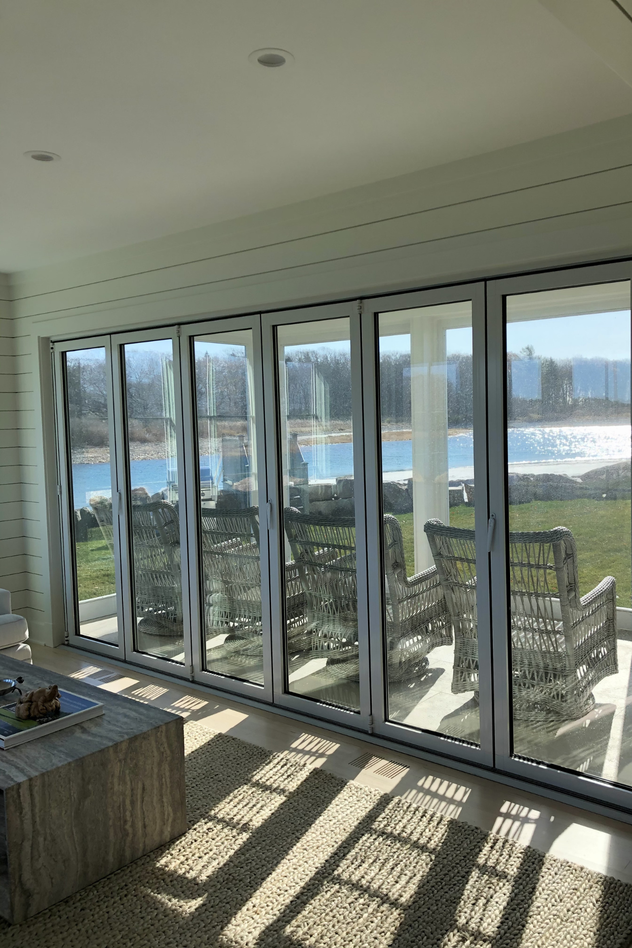 Folding glass doors open to a sunny waterfront view; two wicker chairs on the patio.