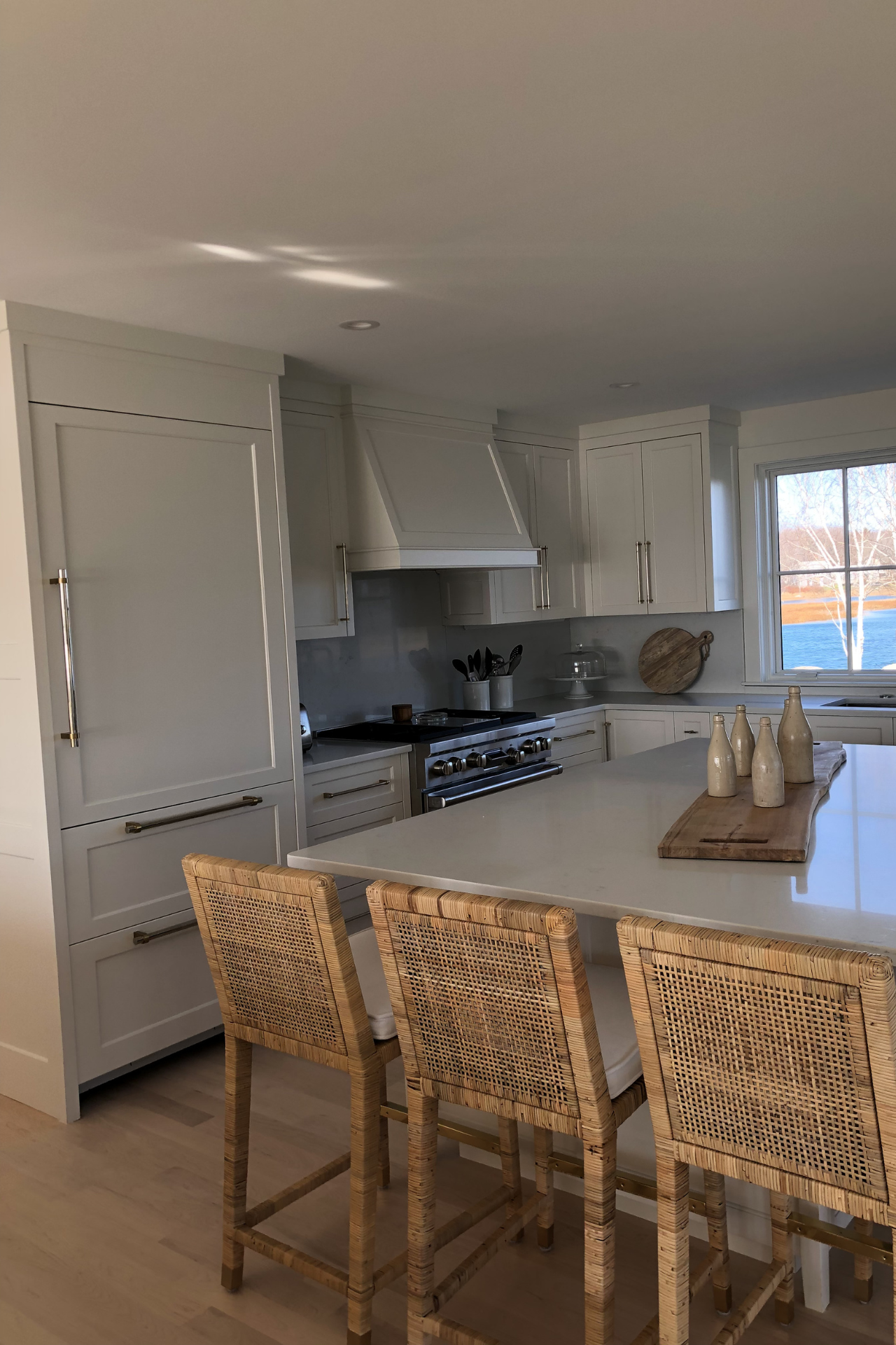 White kitchen with island, stainless steel appliances, and woven bar stools.