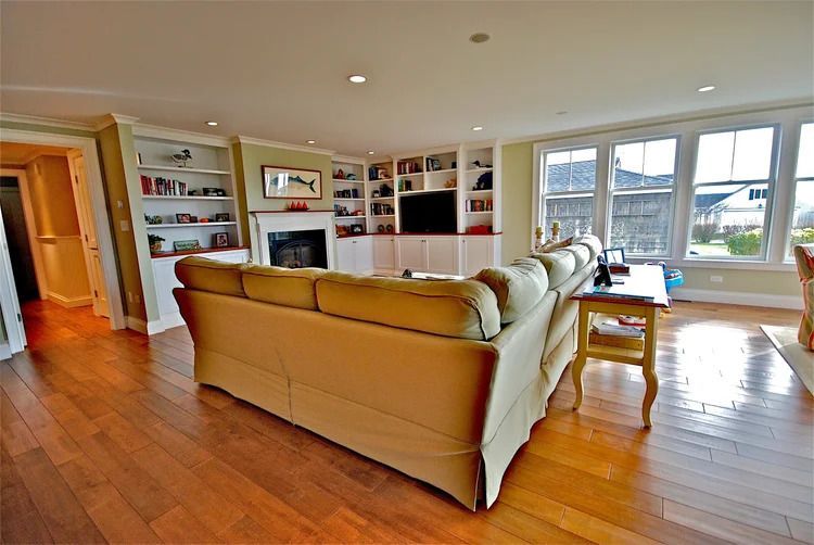 Living room with built-in bookshelves, fireplace, windows, and a tan sofa. Hardwood floors and recessed lighting.
