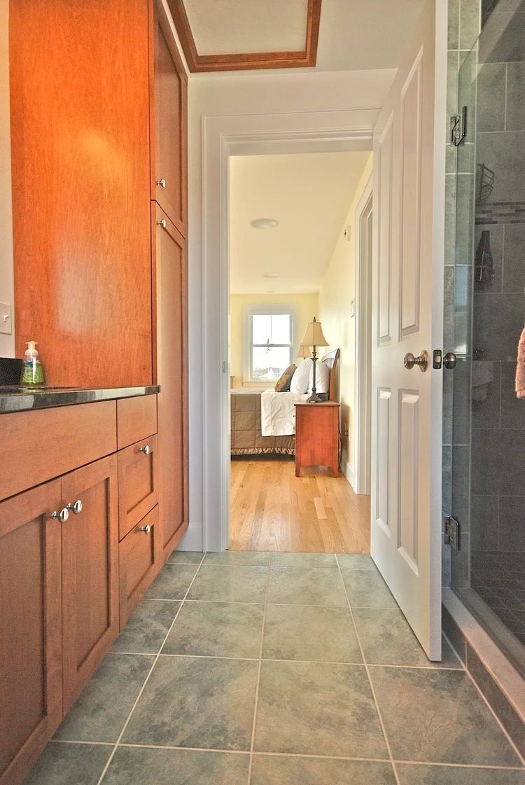Bathroom doorway leading to bedroom with hardwood floors. Bathroom has wood cabinets and green tile.