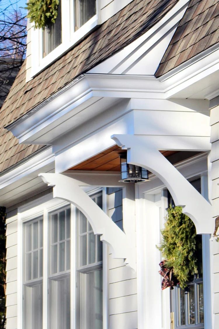 White entryway with ornate brackets, brown roof, and green wreath.