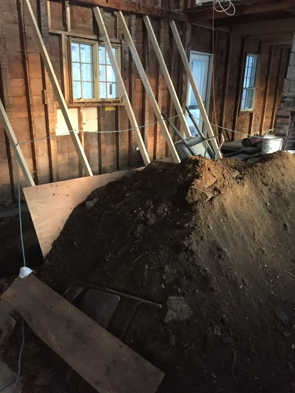 Construction site with dirt pile against a wooden wall and windows, braced by diagonal supports.