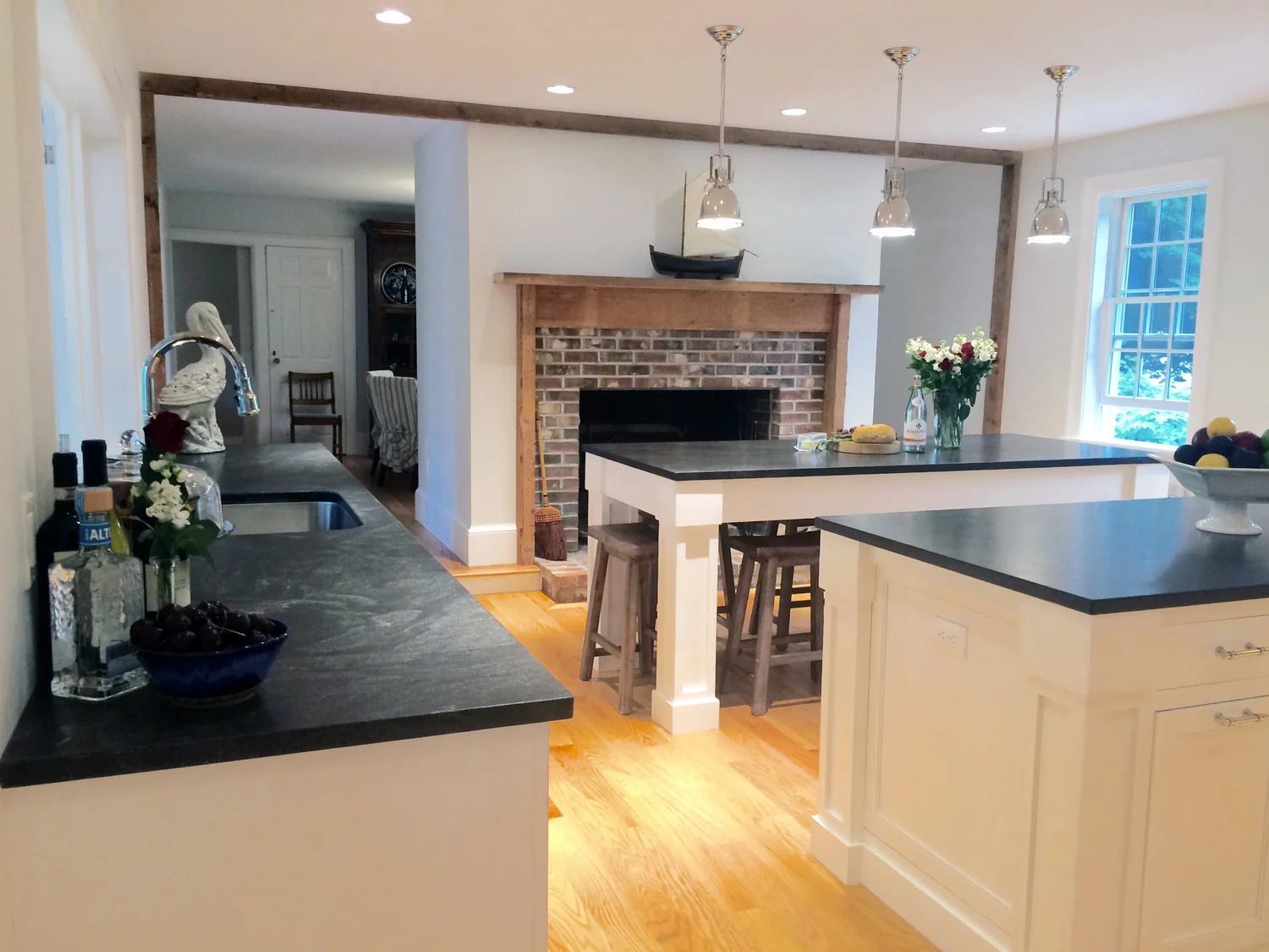 Kitchen with white cabinets, dark countertops, wooden floors, fireplace, and pendant lights.