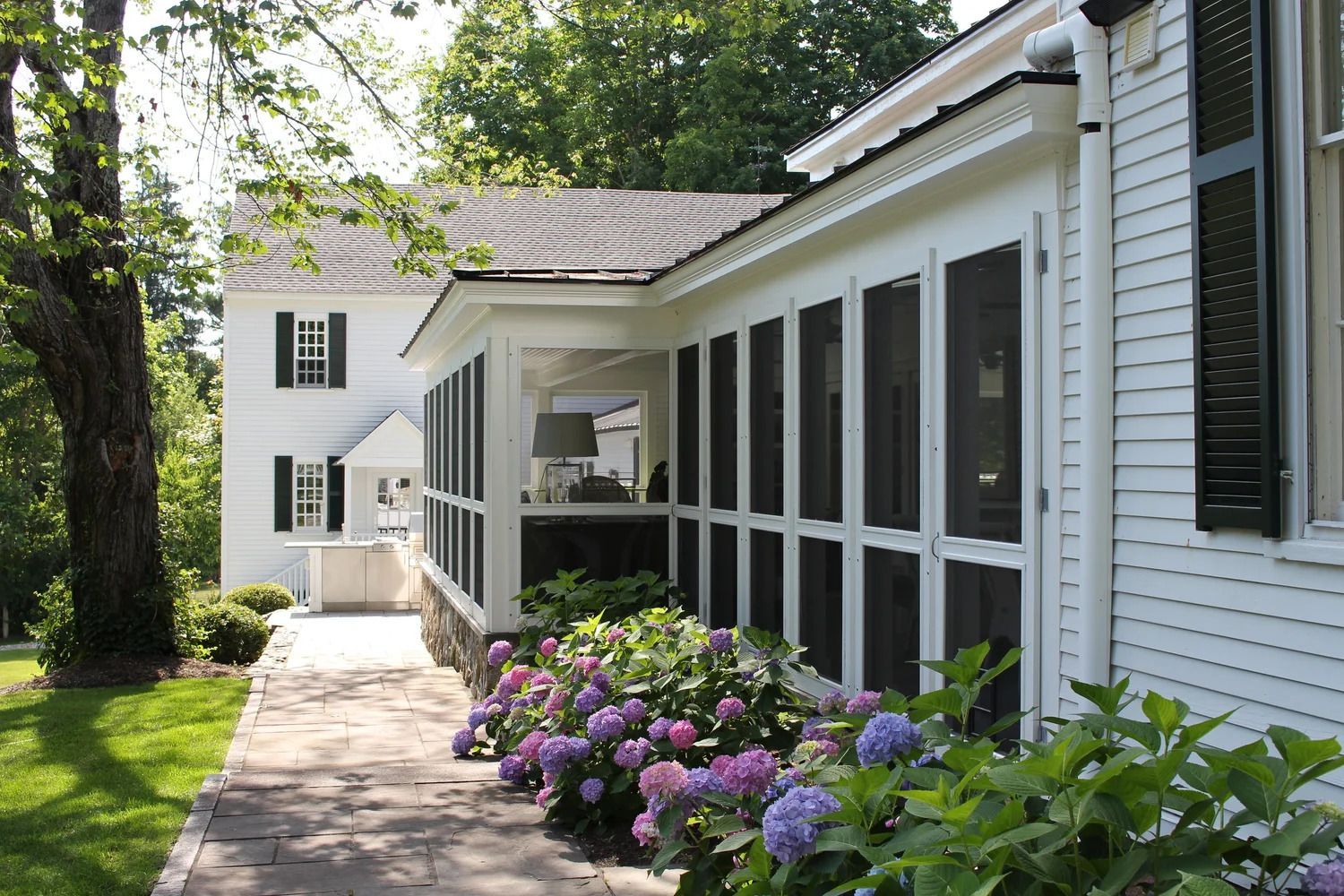 White house with screened porch, stone foundation, and colorful hydrangeas.