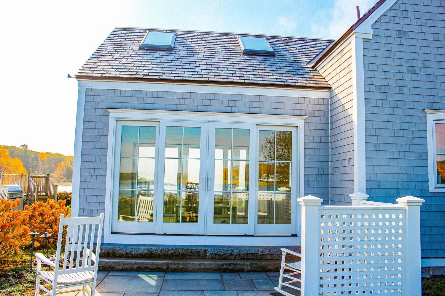 Coastal home exterior with large glass doors and white rocking chairs on a patio.