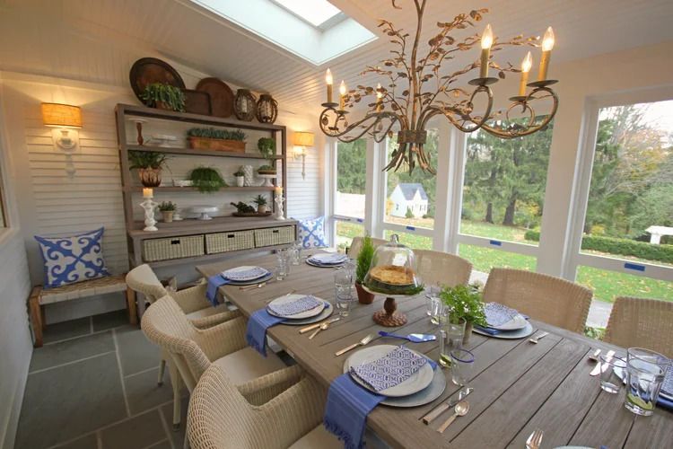 Dining room with a long table, wicker chairs, and a chandelier, overlooking a garden.