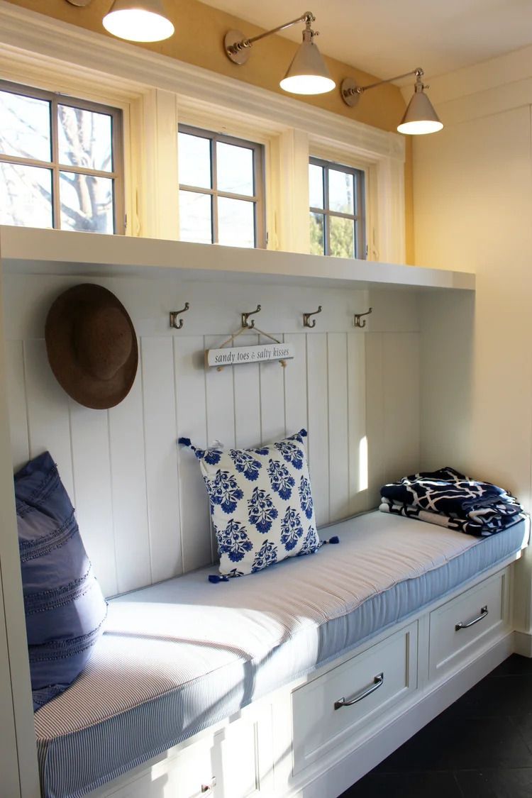 Built-in white bench with blue cushions, hat, and hooks below windows.