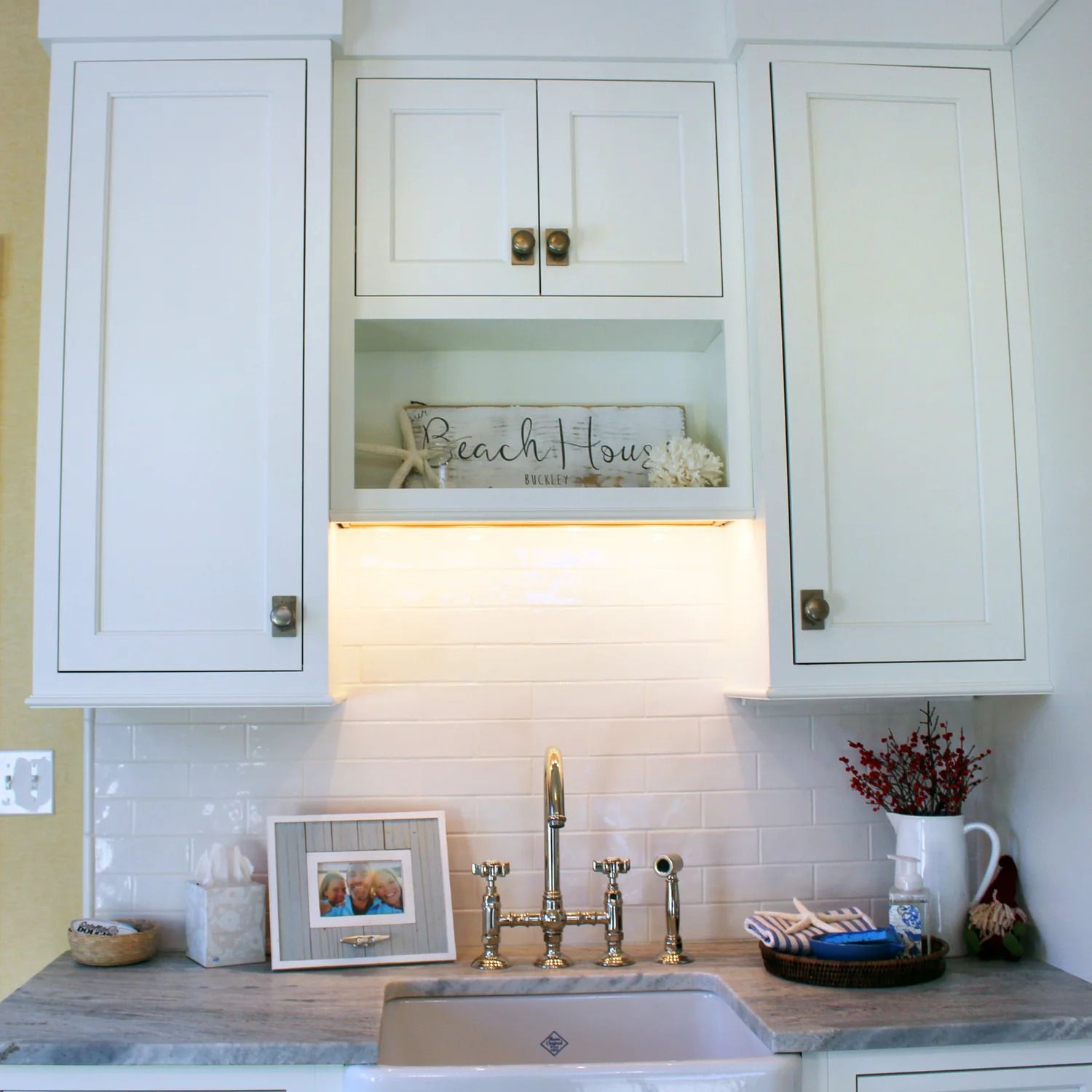 White kitchen cabinets above a farmhouse sink with a tile backsplash and decorative items.