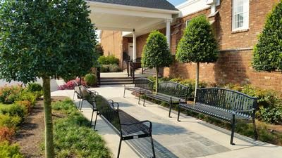 Brick building entrance with benches and a covered walkway beside landscaped shrubs