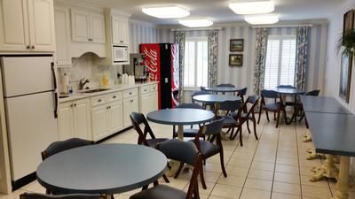 Empty cafeteria with round tables, folding chairs, white cabinets, and a red vending machine.
