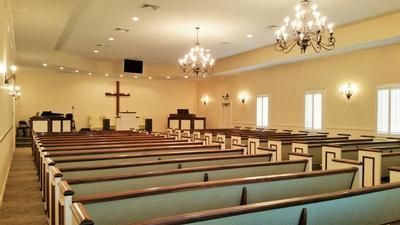 Empty church sanctuary with rows of pews, chandeliers, and a cross at the front
