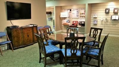 Waiting room with TV, wooden cabinet, and blue-upholstered chairs around a round table.