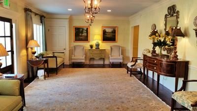 Elegant living room with chandelier, beige carpet, two armchairs, and dark wood sideboard with floral decor