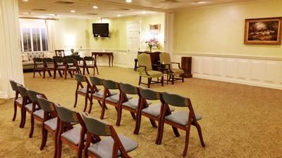 Rows of wooden chairs in a beige meeting room with a TV and wall art at the front