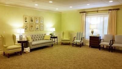 Spacious beige living room with sofa, chairs, lamps, and curtained windows.