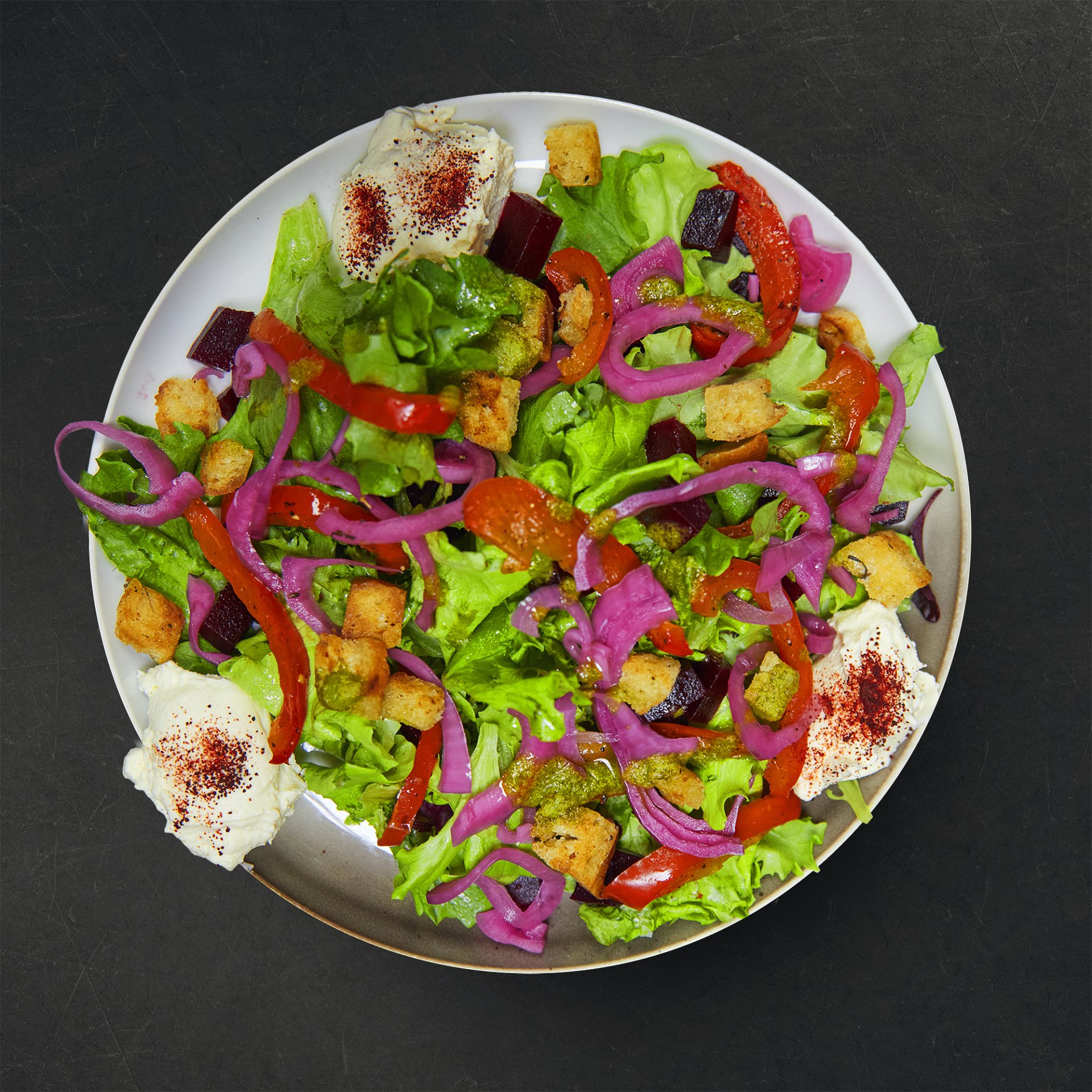 a white plate topped with a salad of vegetables and croutons