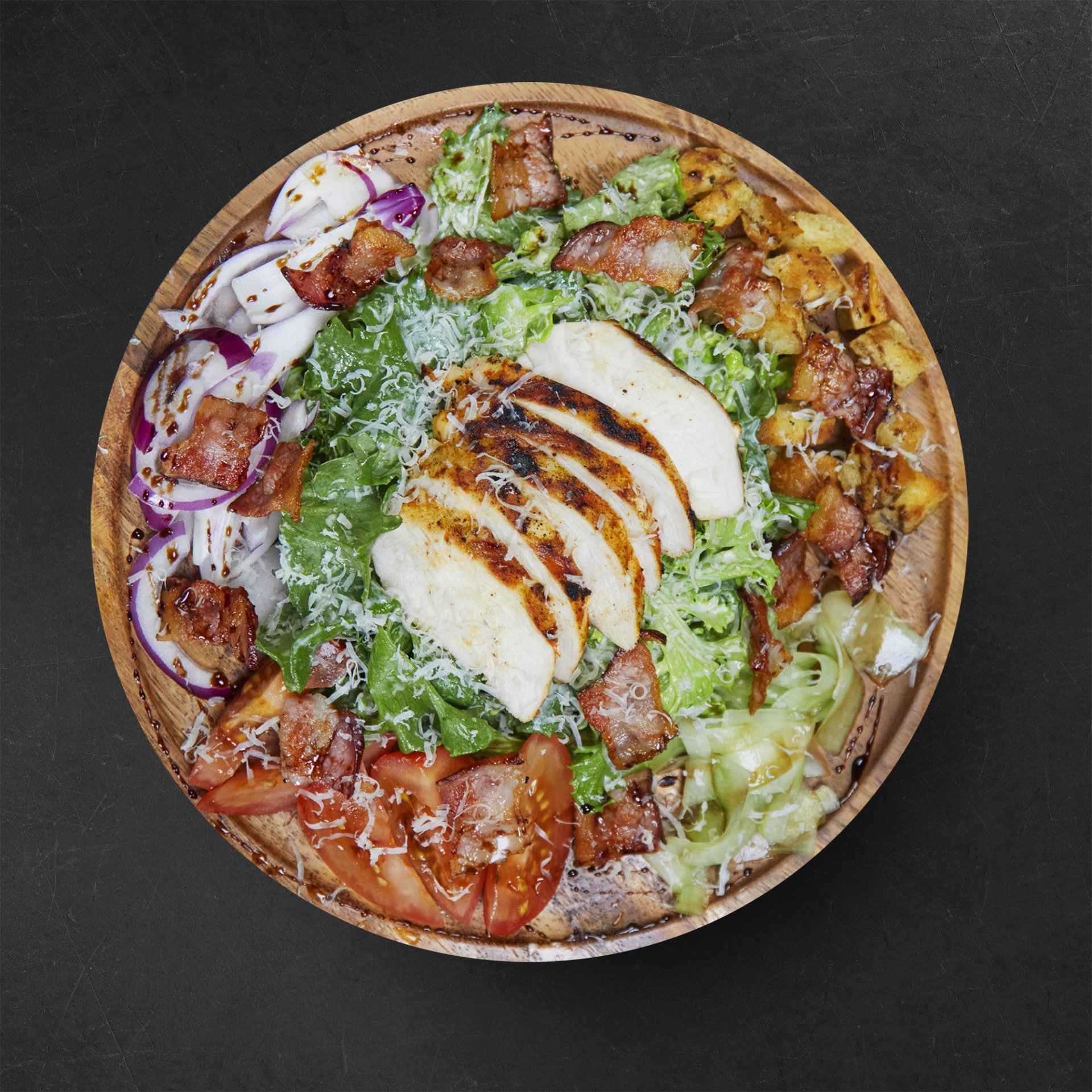 a salad in a wooden bowl with chicken lettuce tomatoes and bacon