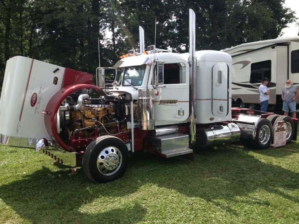 White and red semi-truck with open hood, showing the engine. Parked on grass with a camper in the background.